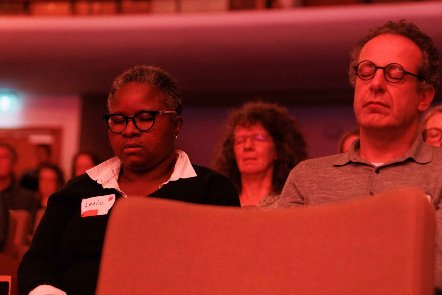 An audience sitting in red-tinted lighting during a presentation or performance.