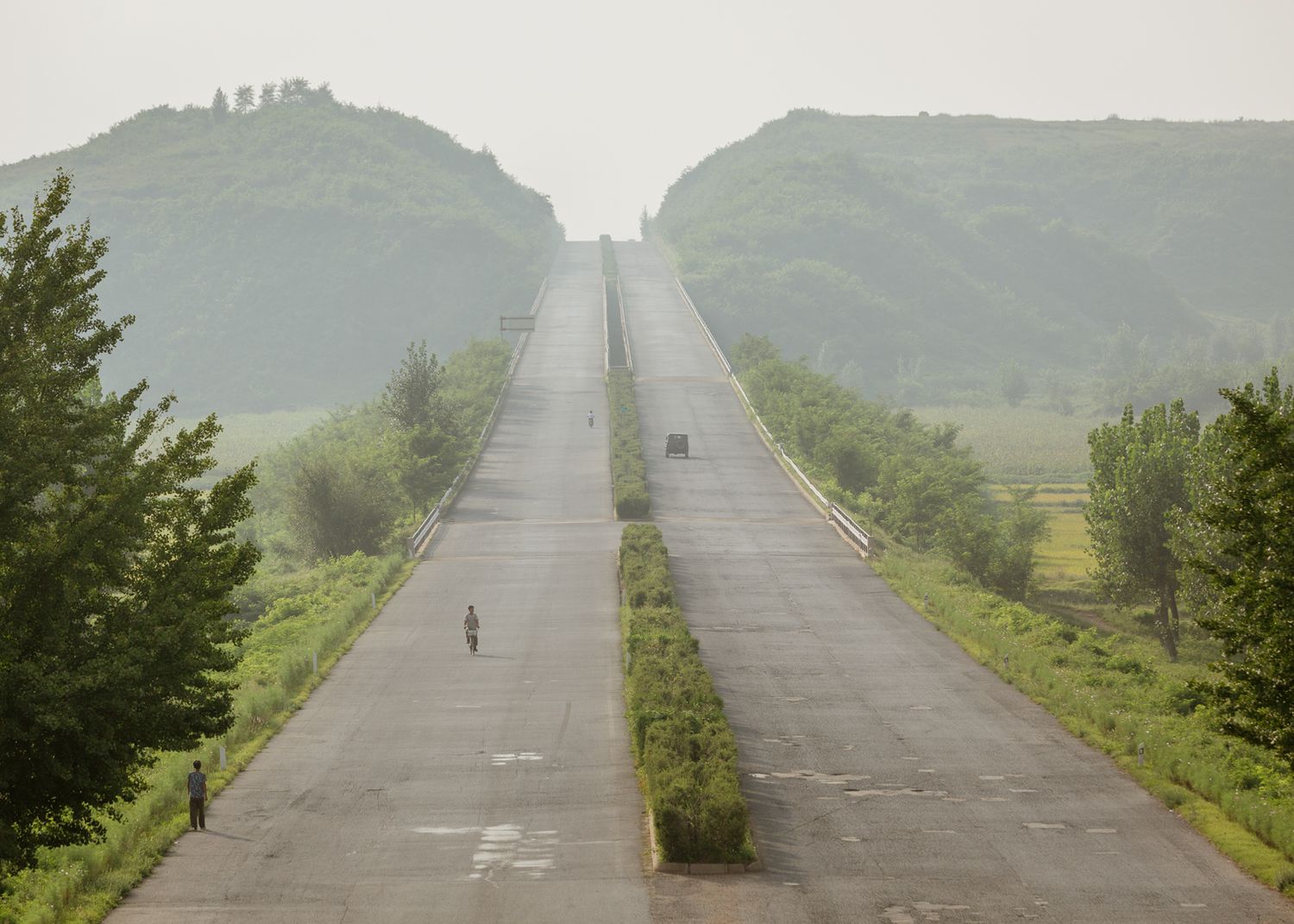 Long straight highway stretching into misty mountains with sparse traffic.