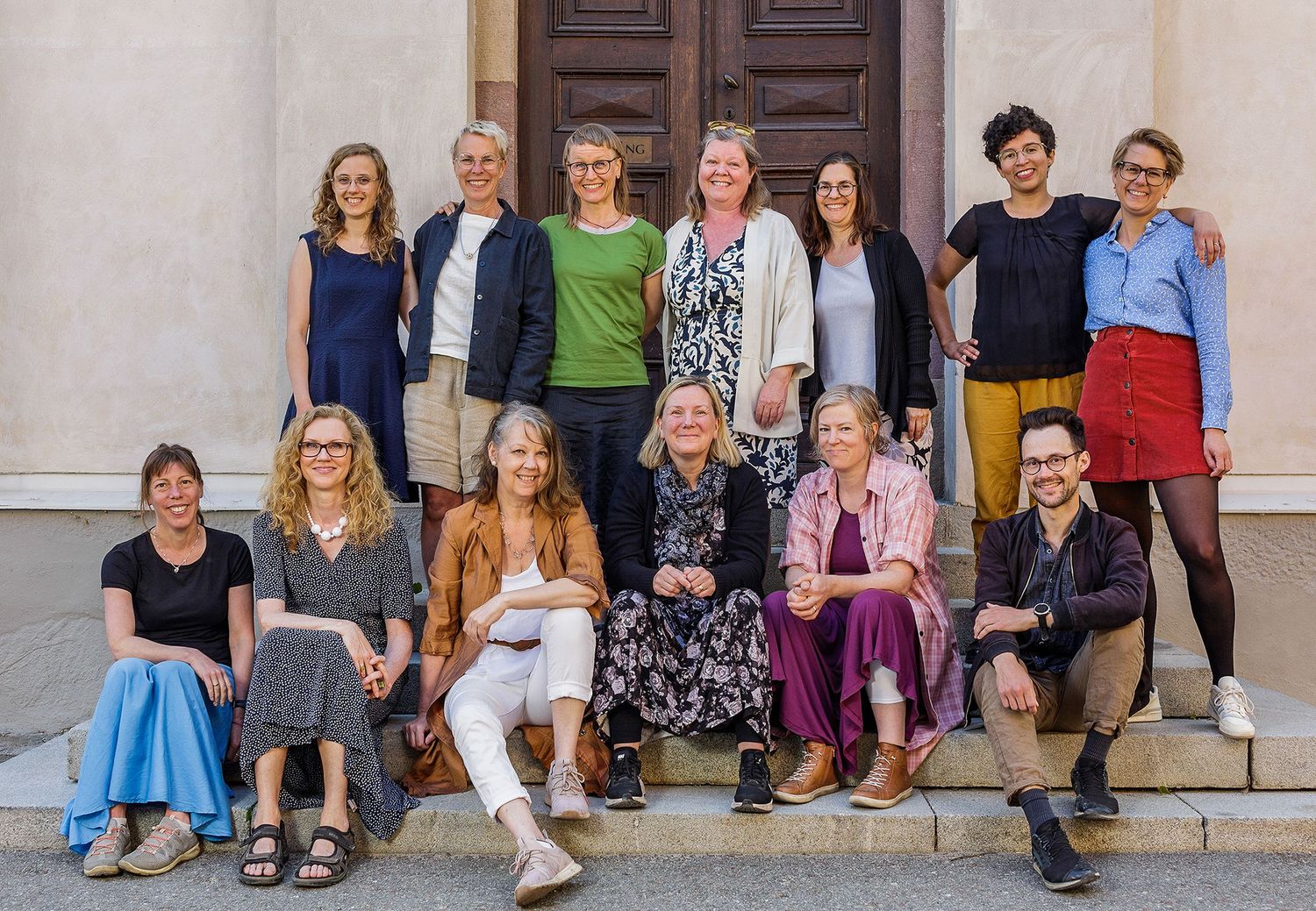 Stort gruppfoto av personer sittande på stentrappor utomhus framför byggnadens entré