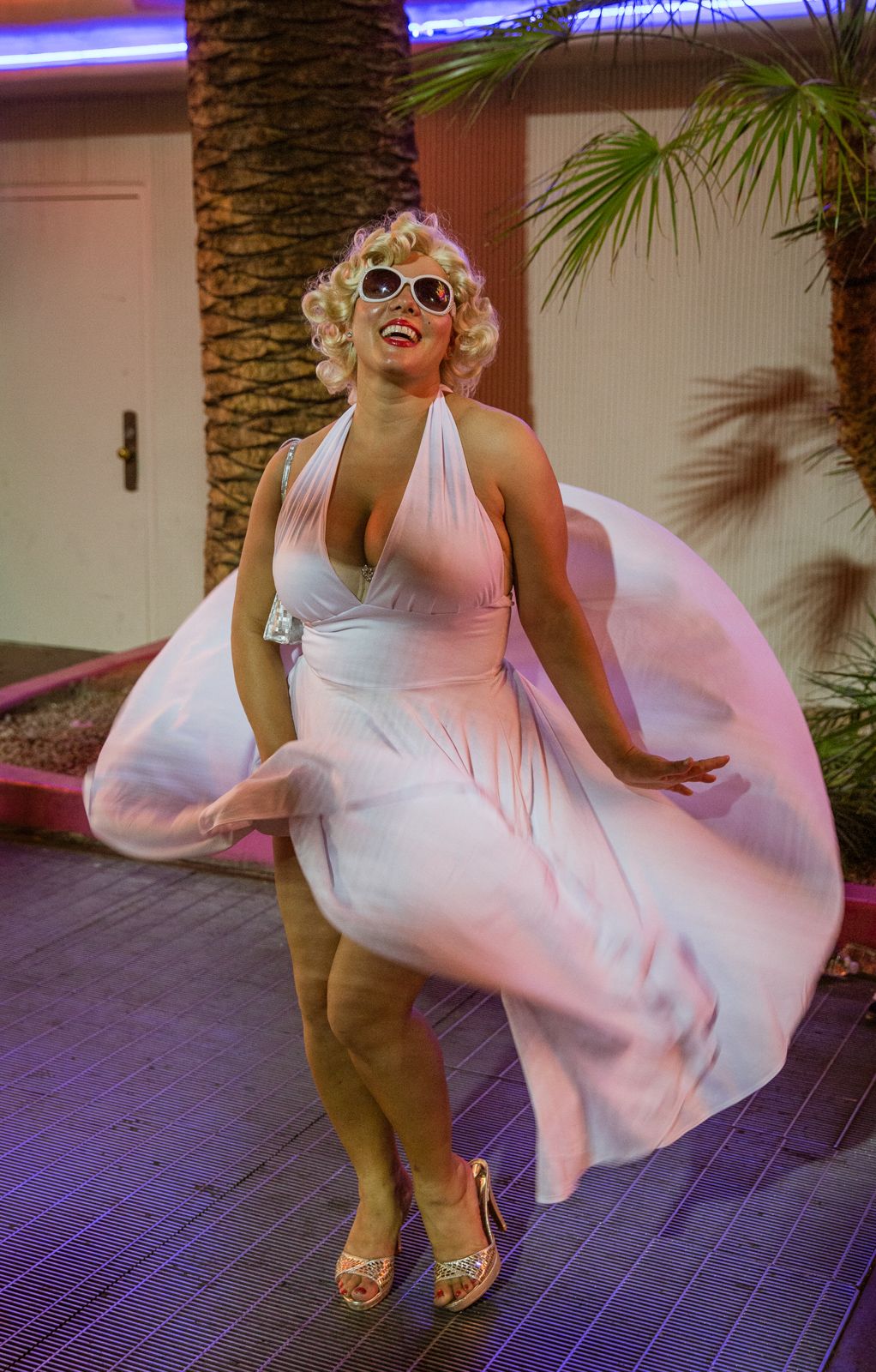 Figure in flowing white dress twirling playfully under palm trees.