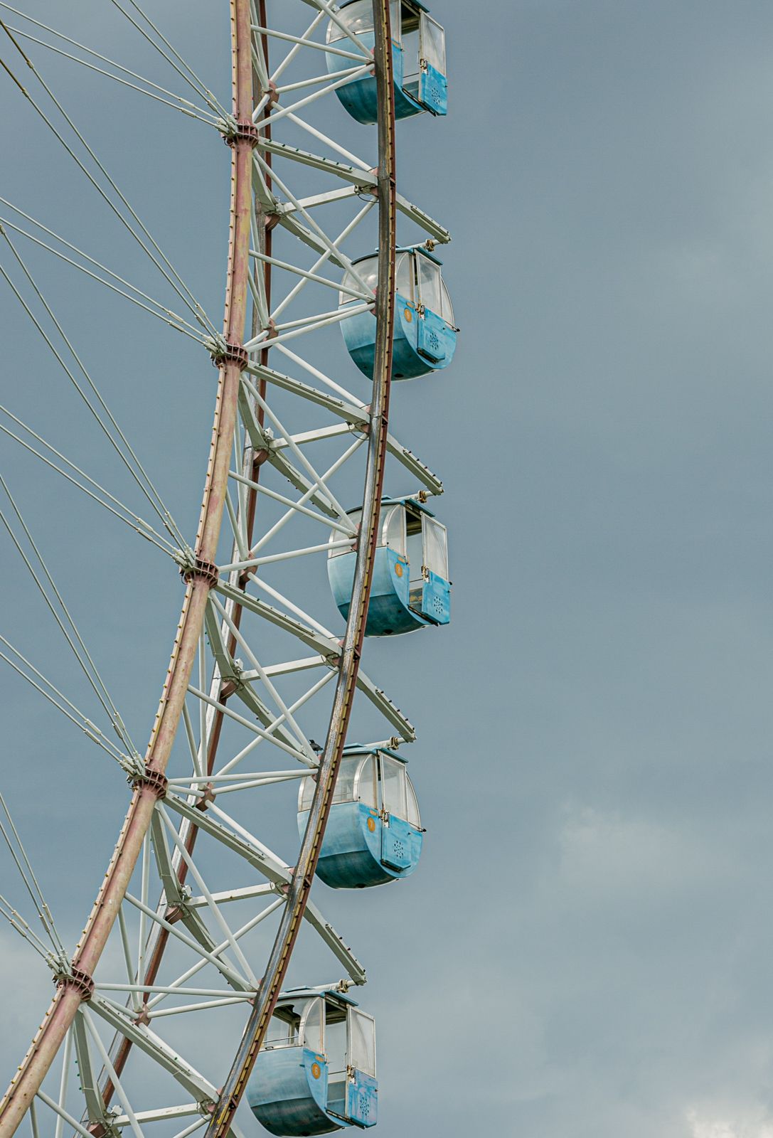 Close-up view of blue and white Ferris wheel gondolas against cloudy sky.