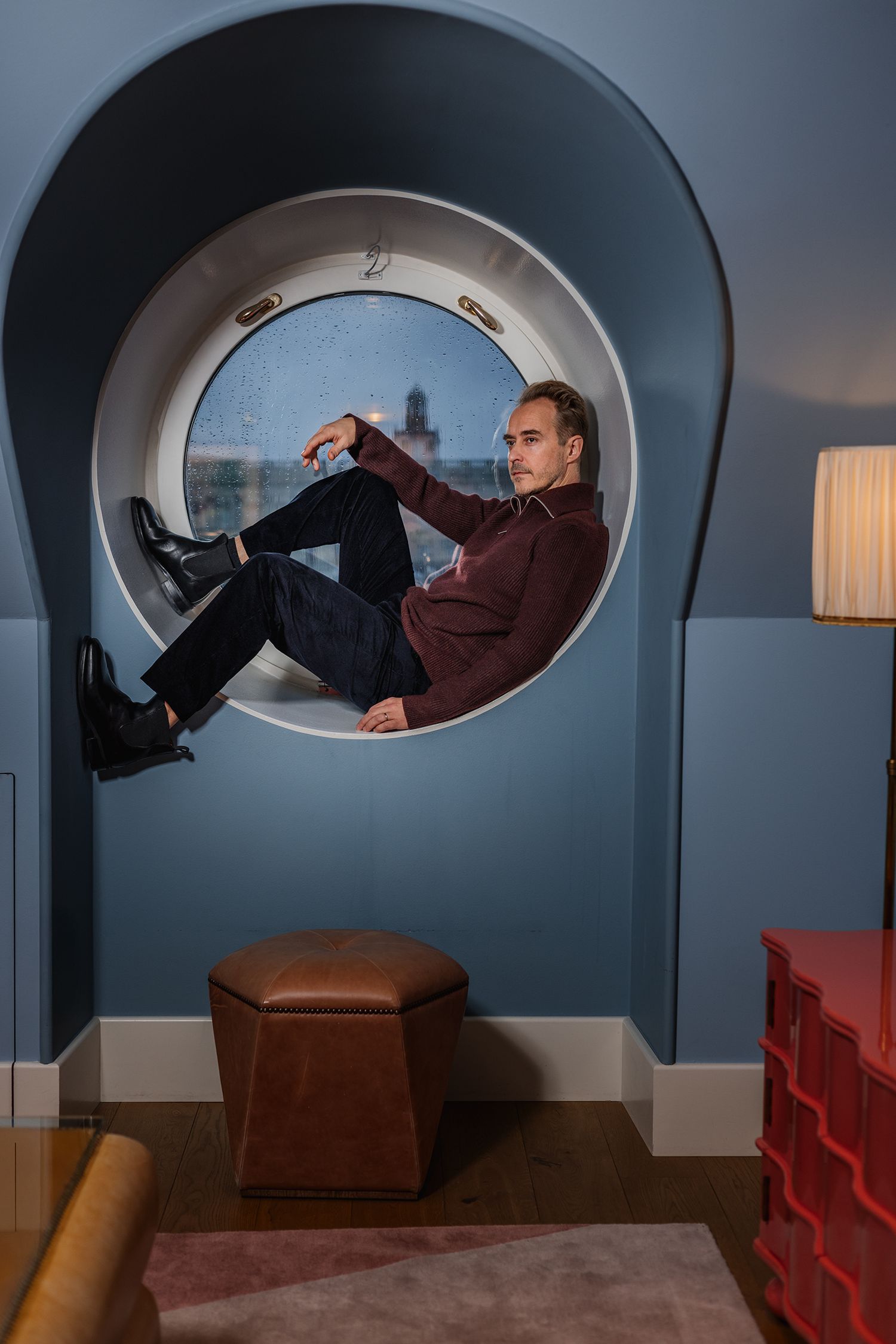 Person lying in a curved architectural alcove with blue walls and modern furniture.