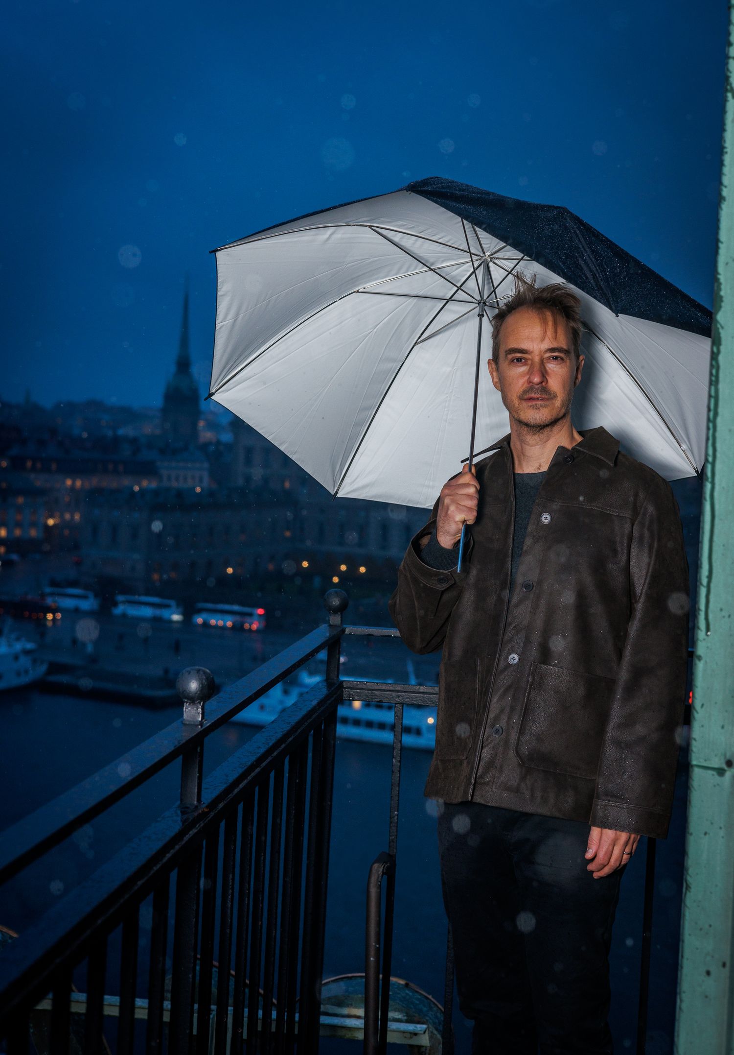 Person with white umbrella standing on balcony against blue twilight cityscape.