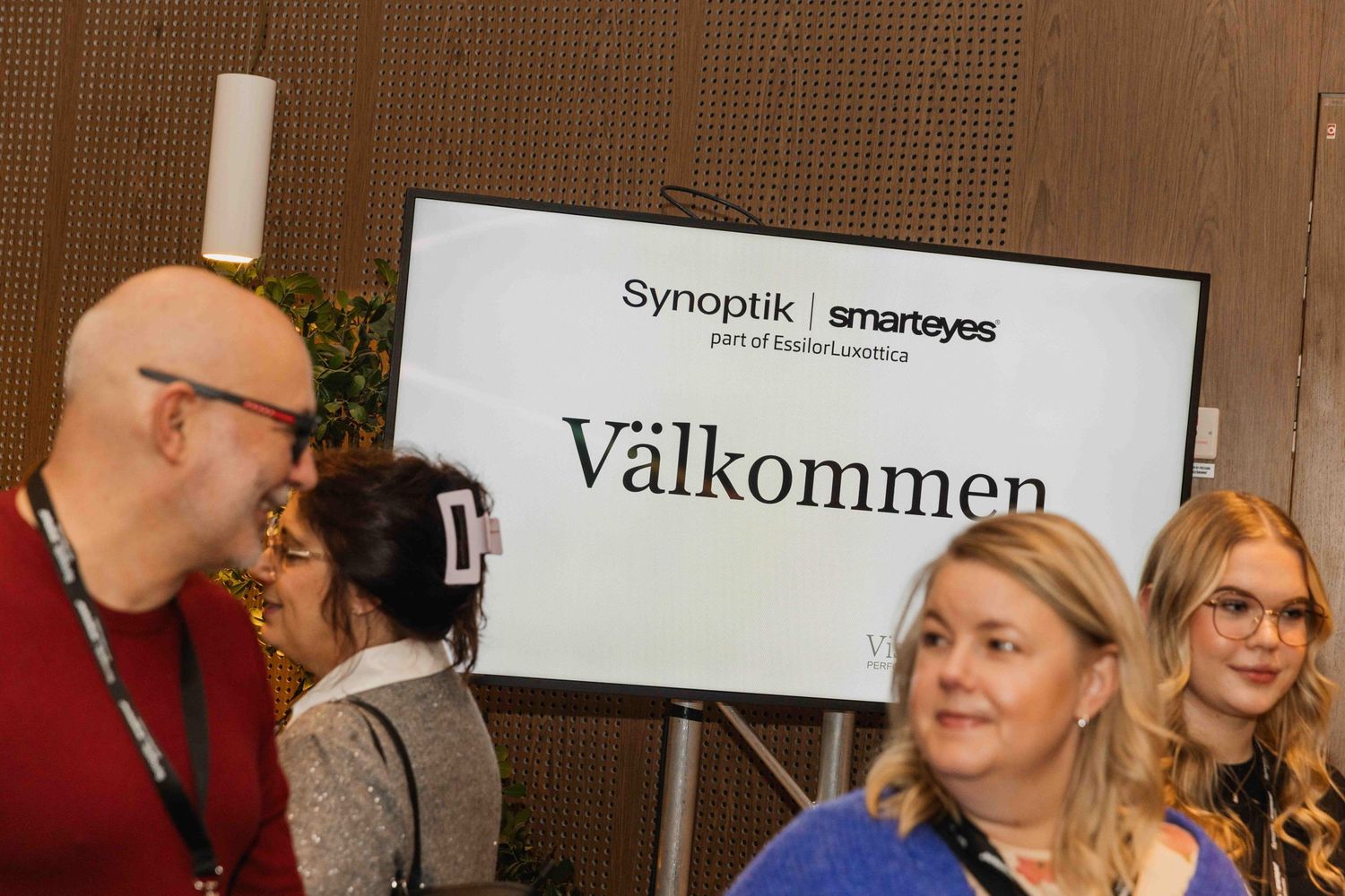 Business conference attendees networking in a brightly lit venue with signage and displays.