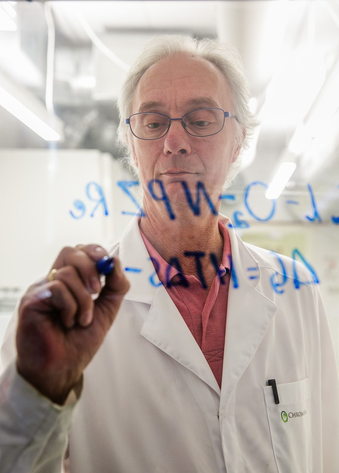 Person in lab coat writing on transparent surface in scientific setting.
