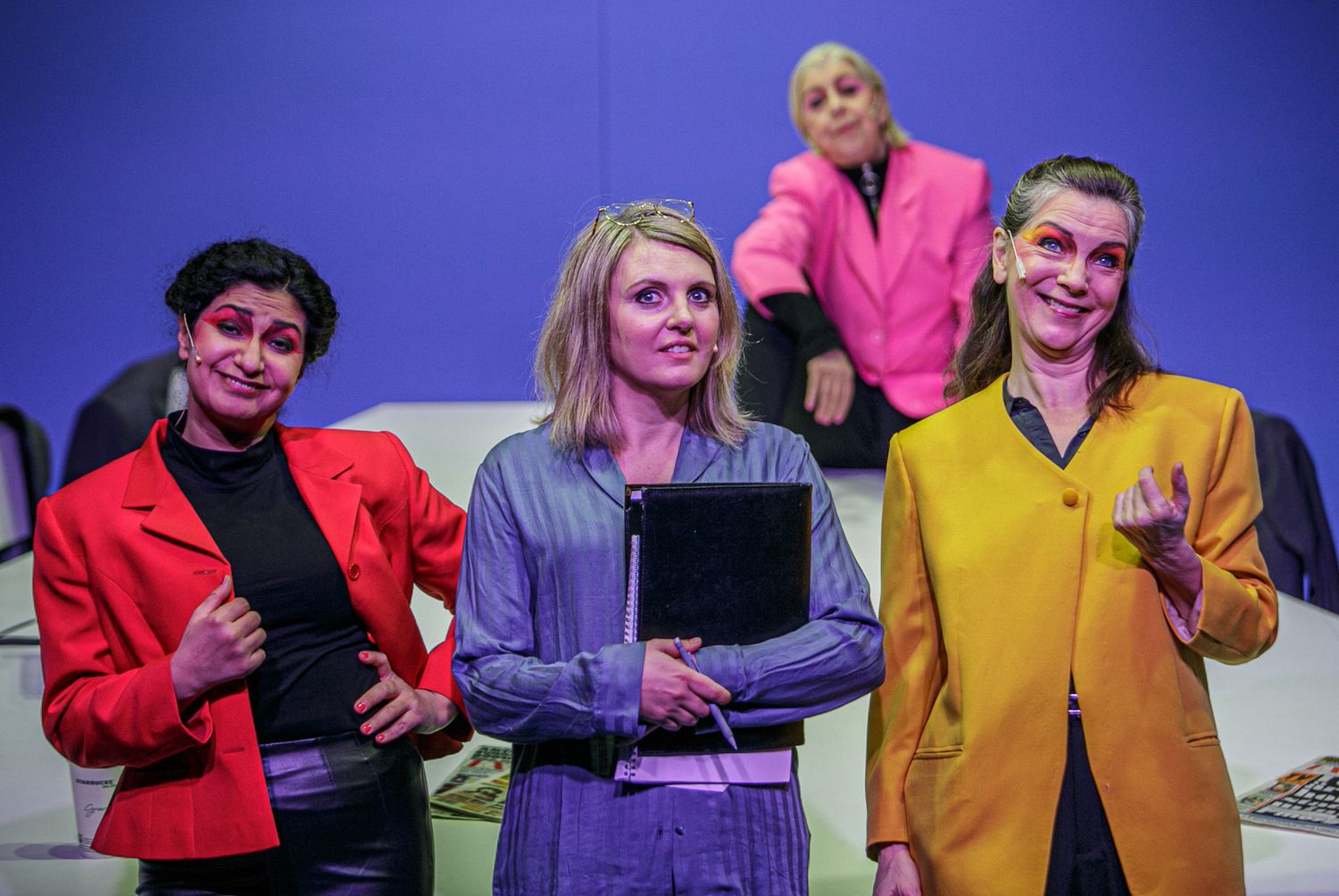 Performers in vibrant colored outfits gather on stage with blue lighting backdrop.
