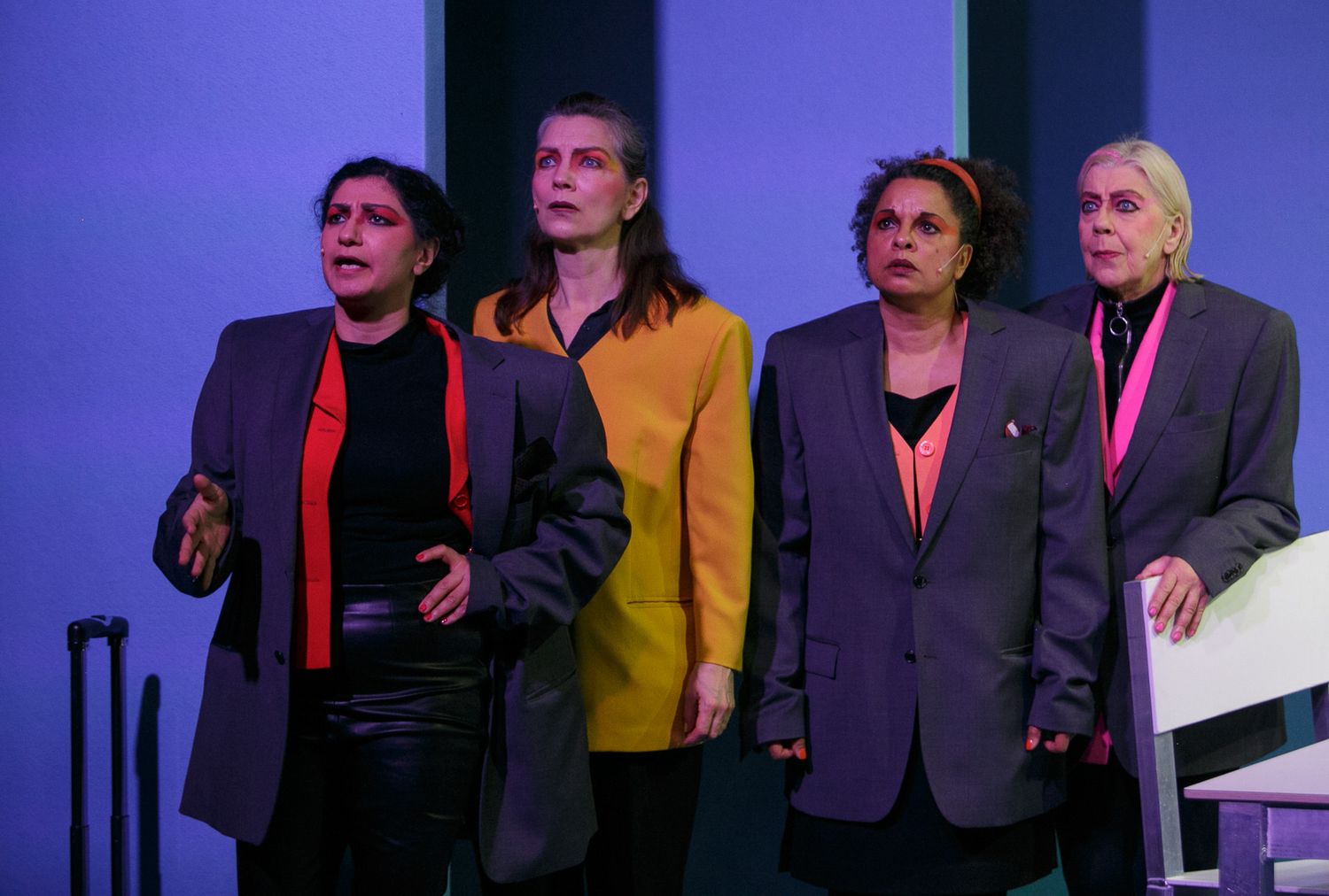Theater ensemble cast standing together on stage with blue lighting and dramatic shadows.