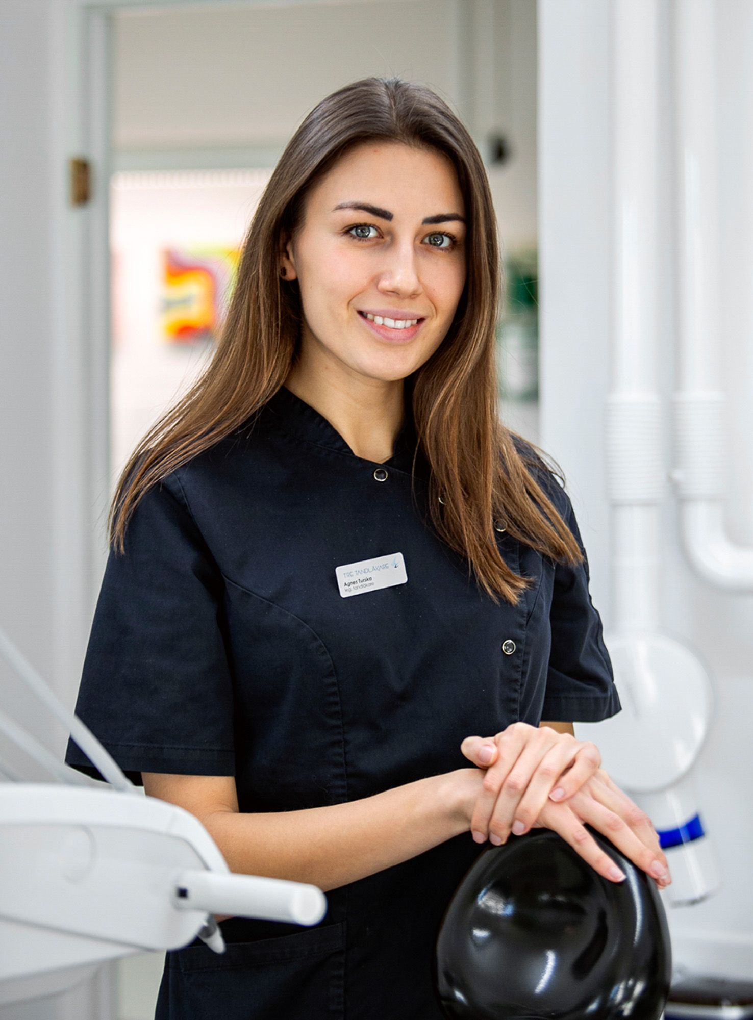 Dental professional in black scrubs posing next to dental chair in modern clinic.