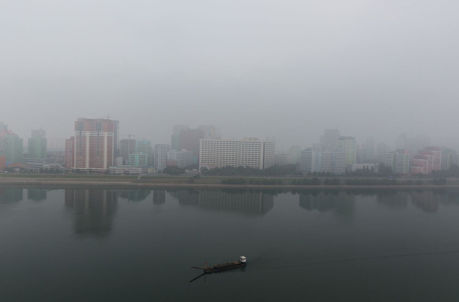 Foggy cityscape view of Pyongyang showing modern buildings through the haze.