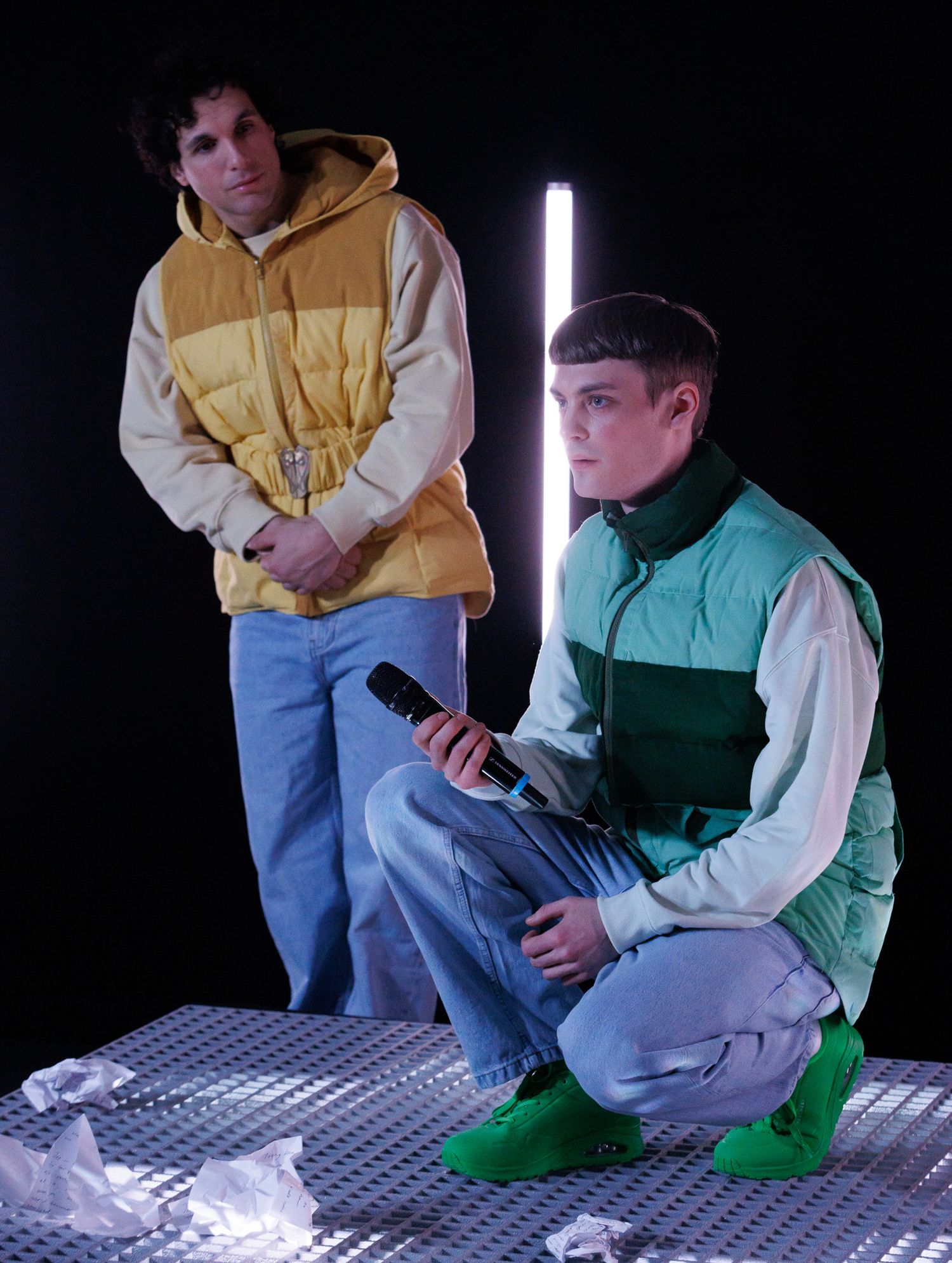 People in casual attire sit on reflective surface under dramatic lighting.