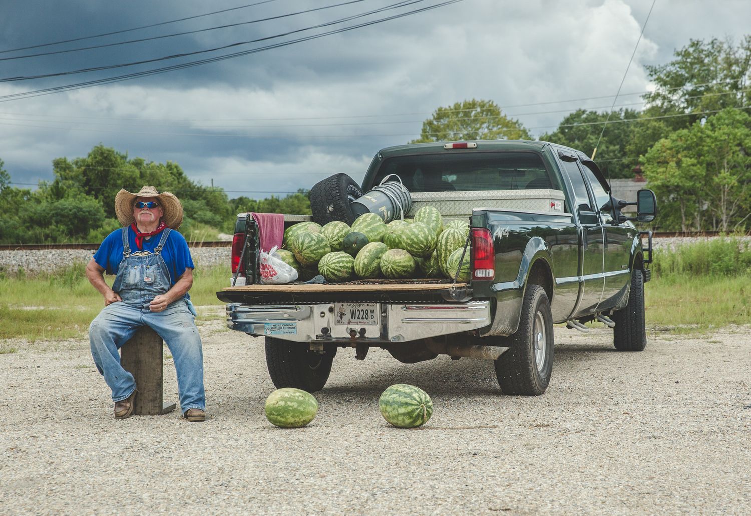 Pickup trucks parked at outdoor market with watermelons displayed for sale.