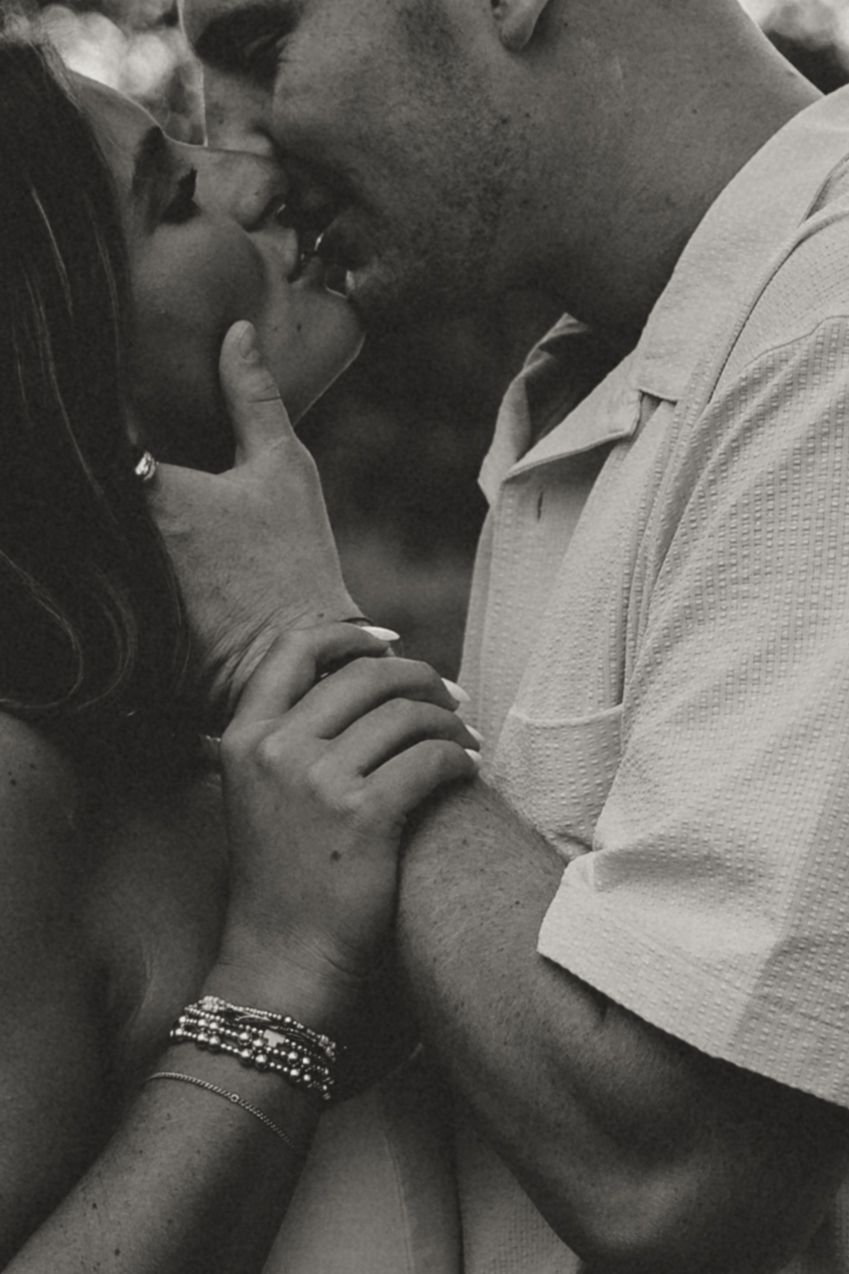 Black and white photo of a couple sharing a romantic kiss, woman wearing bracelets and ring, man in textured shirt.