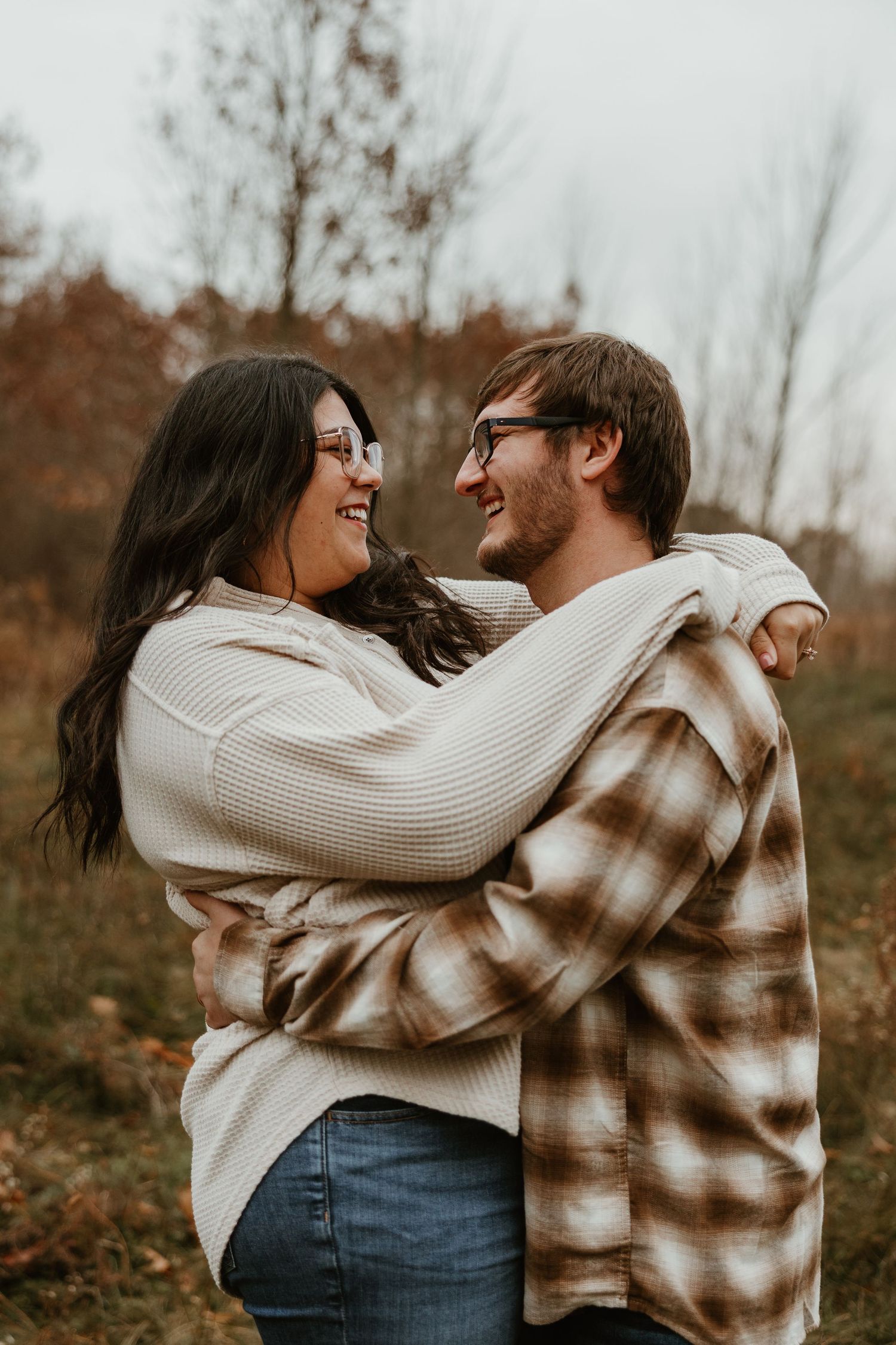 A couple embraces and smiles at each other outdoors in autumn, wearing cozy plaid and knit sweaters.