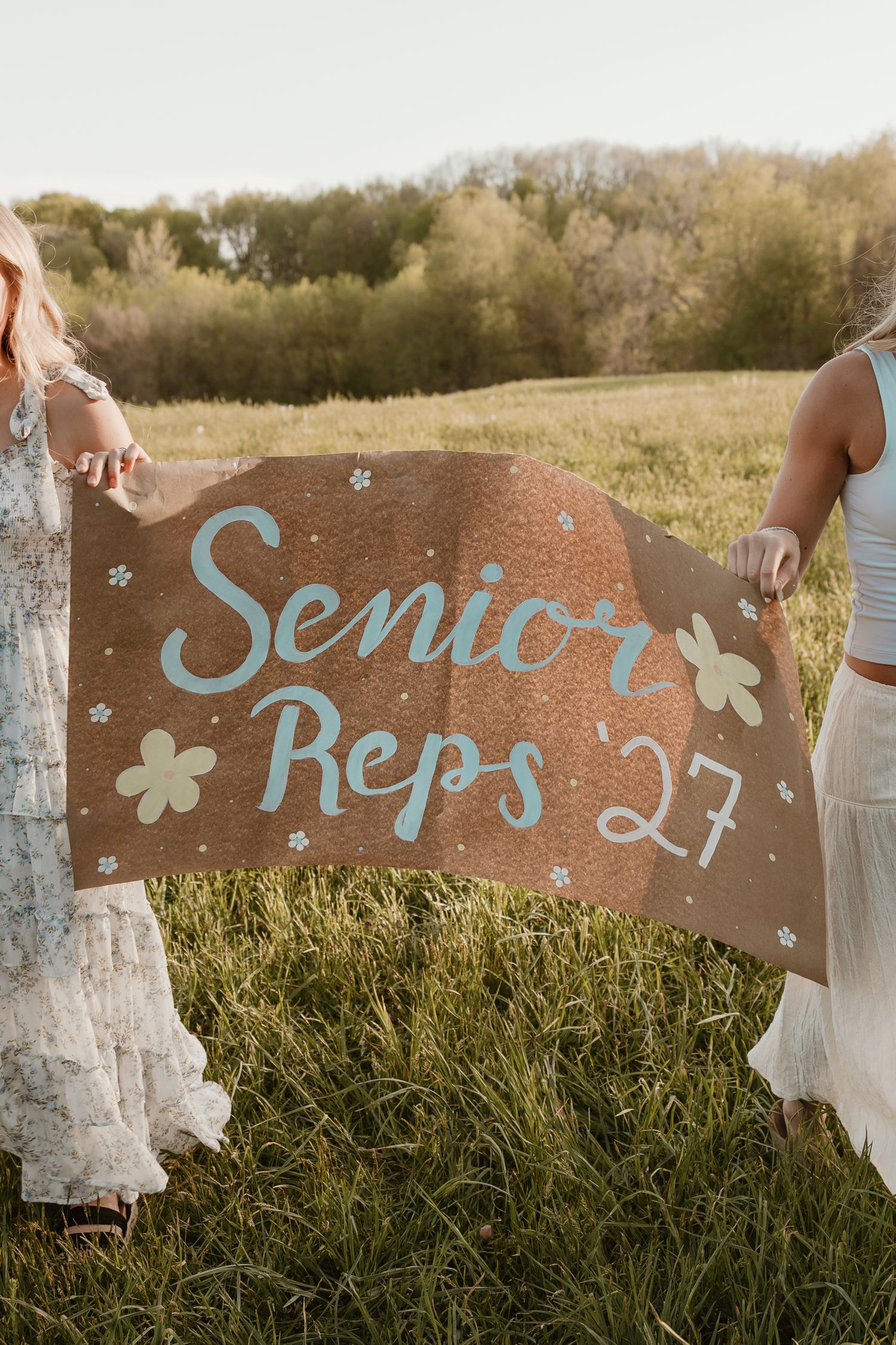 Two girls holding a Senior Reps '27 banner in a grassy field outdoors.