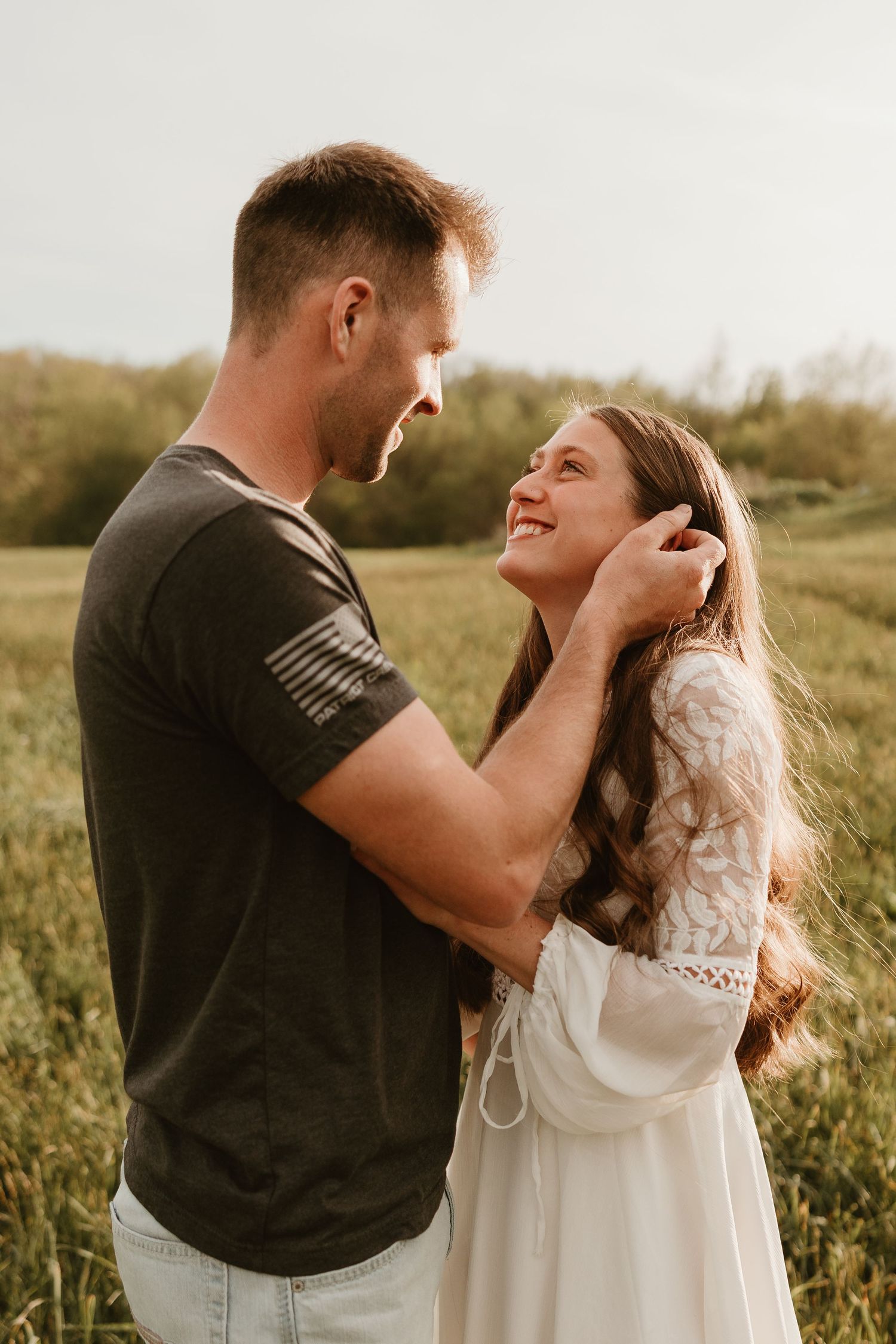 A couple shares a romantic moment in a sunlit field, the man tenderly brushing hair from the smiling womans face.