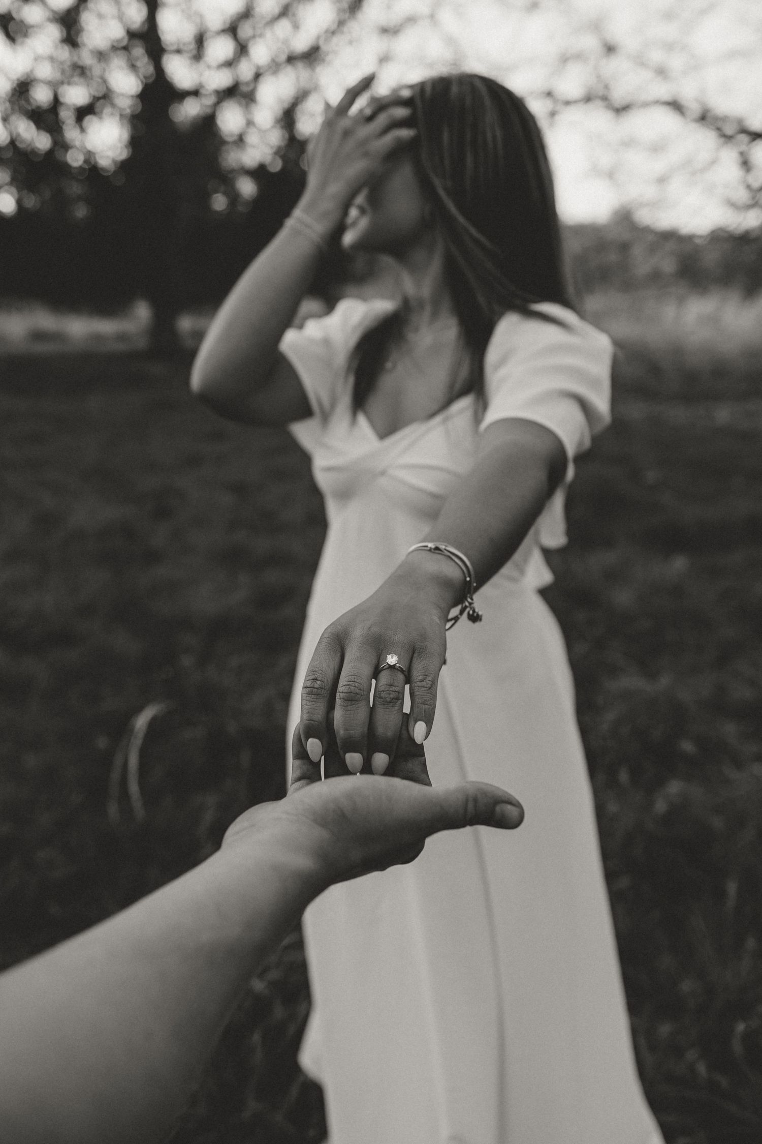 Black and white photo of a bride in white dress reaching out her hand showing engagement ring to her partner.