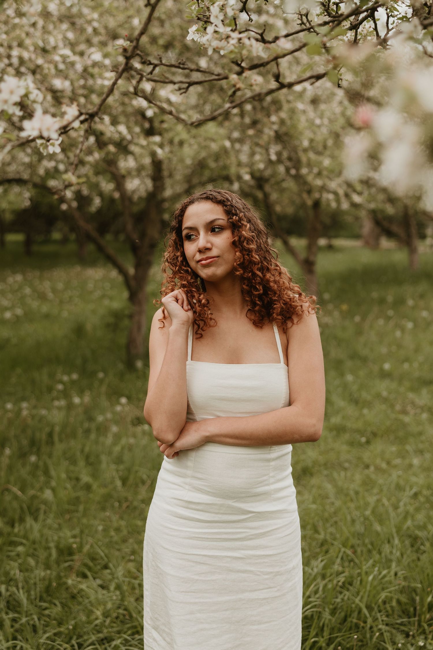Woman in white dress standing under blooming trees in a garden.