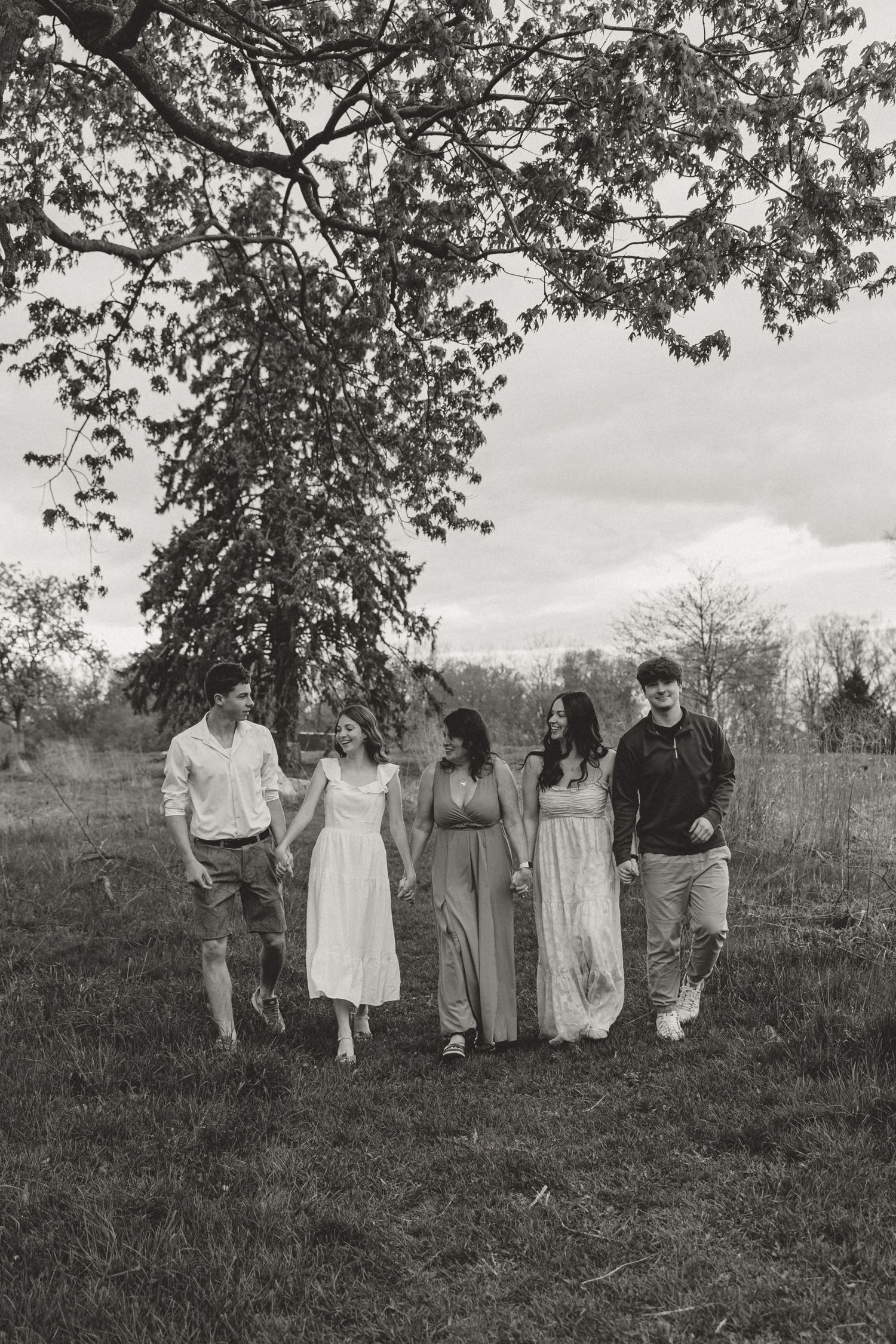 Black and white photo of five friends walking together under a large tree in a grassy field.