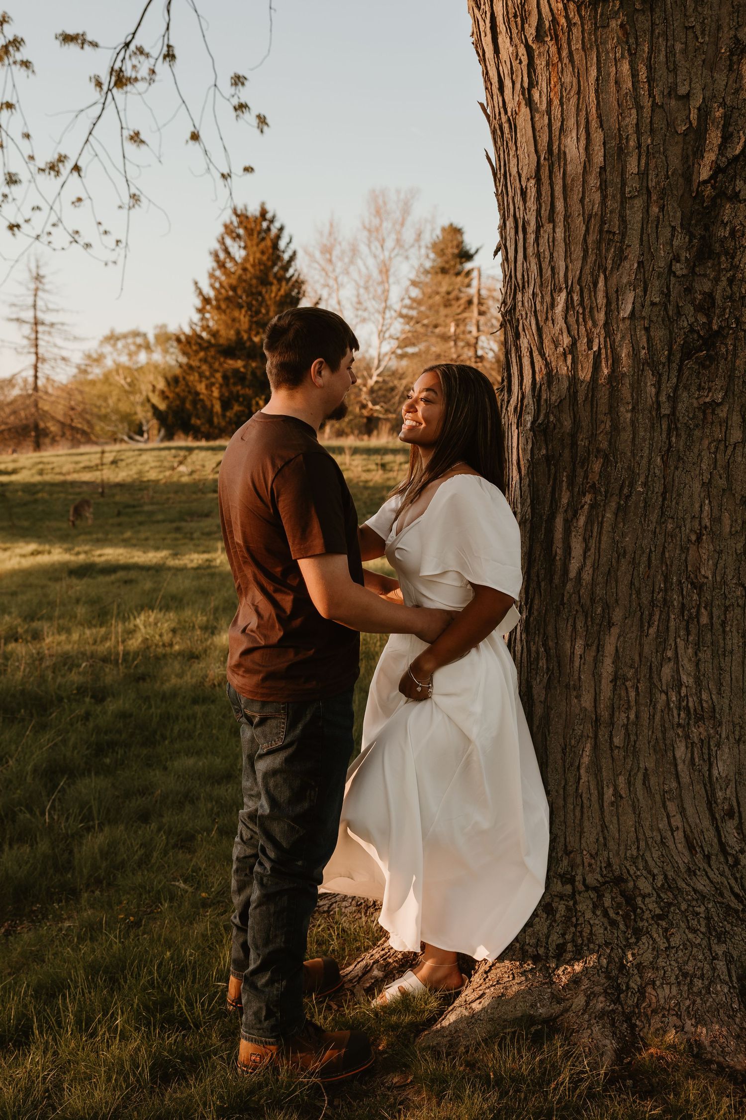 Couple sharing a romantic moment leaning against a tree at golden hour in a lush green park.