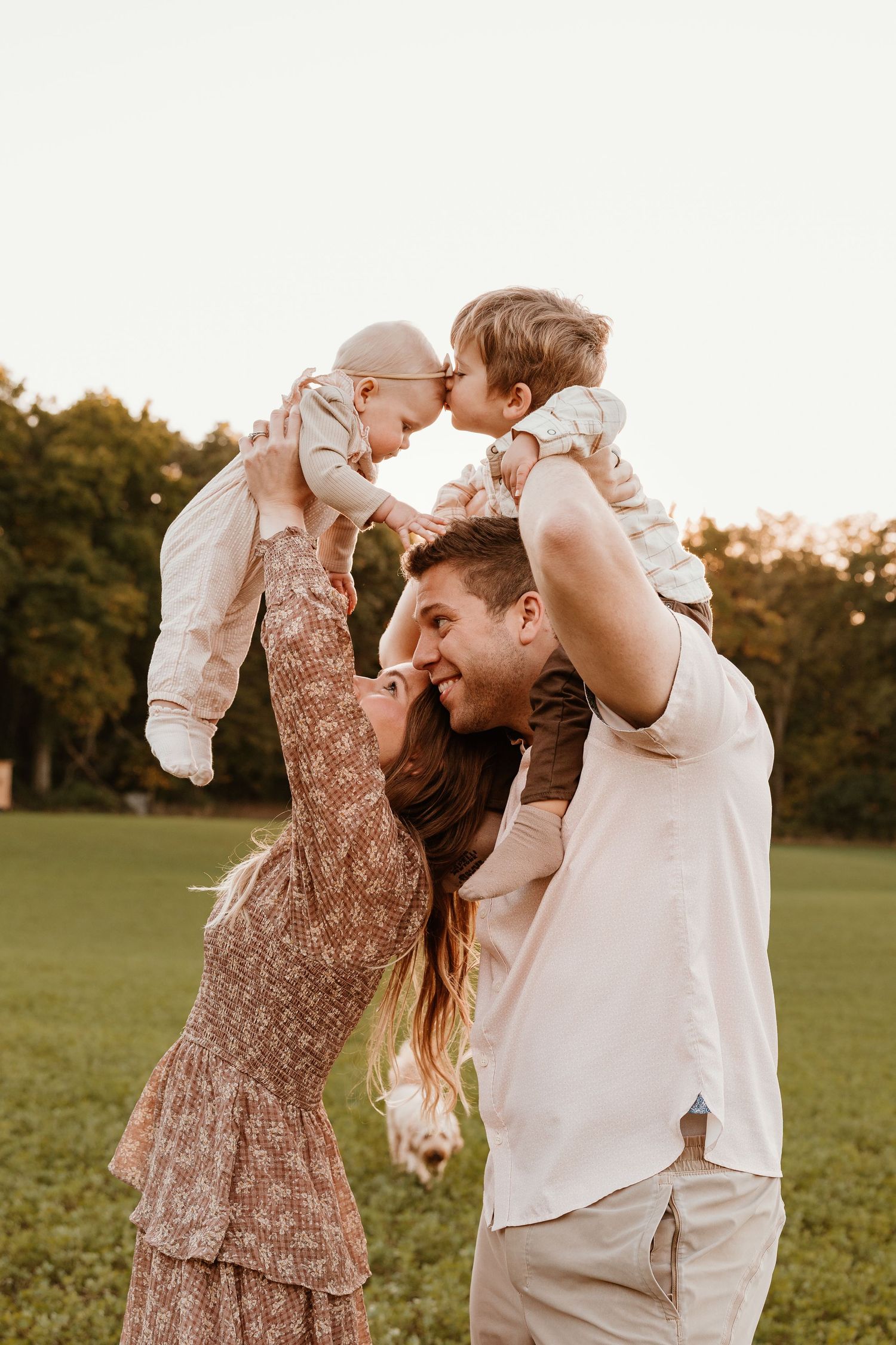 Happy family with two young children enjoying a sunny outdoor moment in a green field at golden hour.