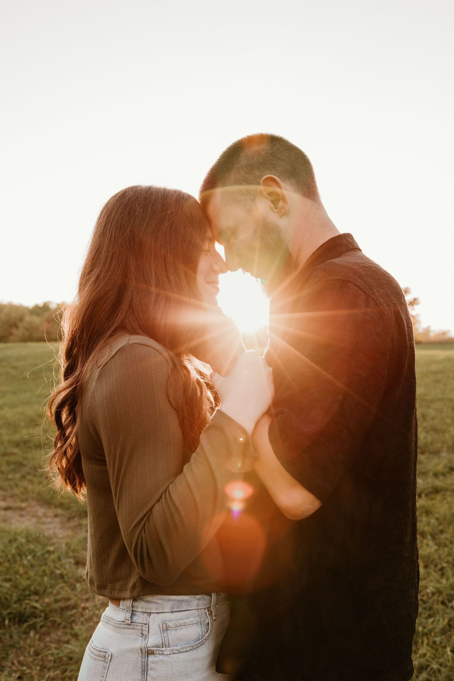 Couple sharing a romantic sunset moment in a field, golden backlight creating a beautiful lens flare between them.