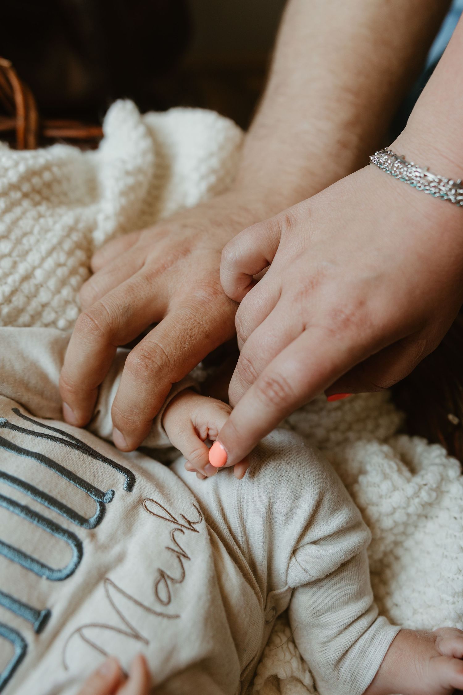 Adult hands gently holding a newborn baby's tiny hand, with the infant wearing a personalized outfit named Mark.