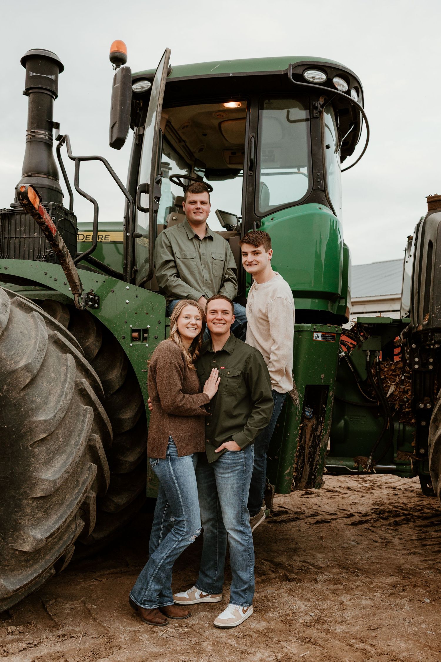 Family of four posing in front of a green John Deere tractor on a farm, wearing casual earth-tone outfits.