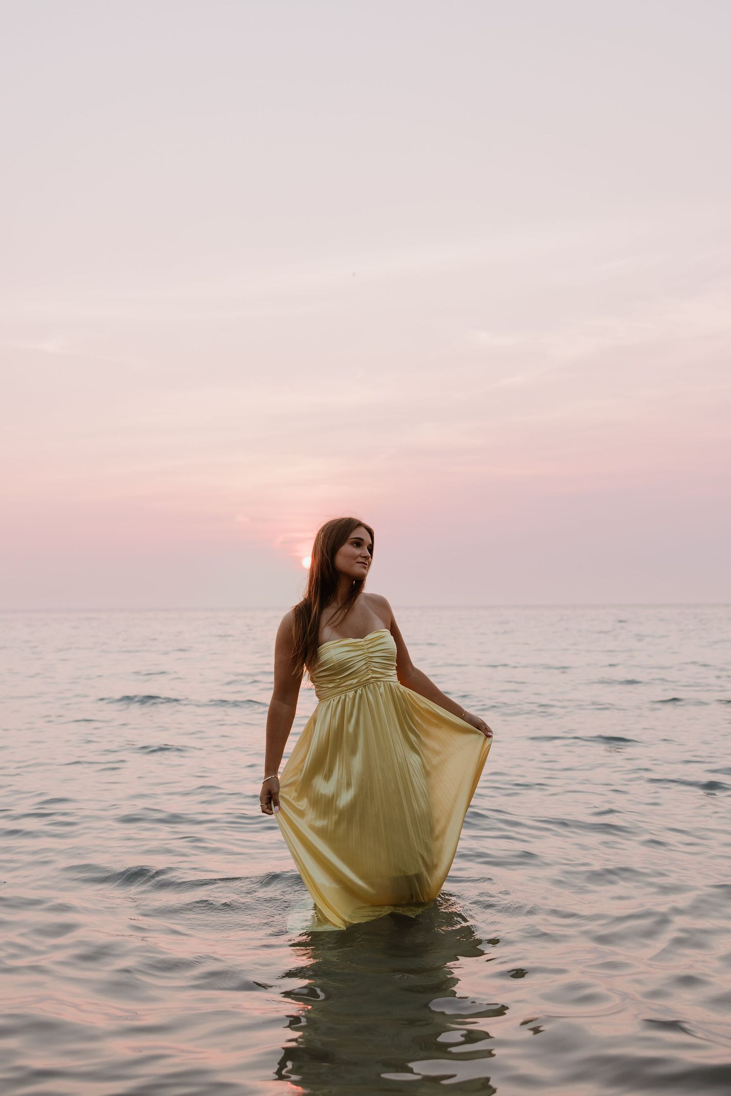 Woman in yellow maxi dress wading in ocean at sunset.