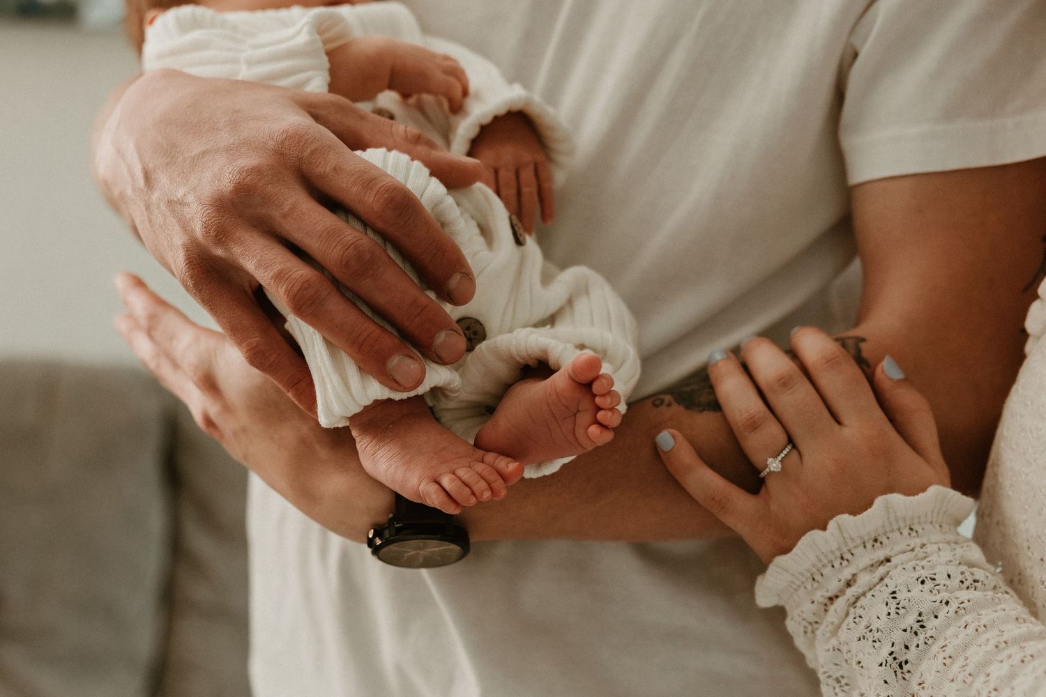 Parents tenderly holding newborn baby feet and tiny hands in a warm, intimate close-up photo.