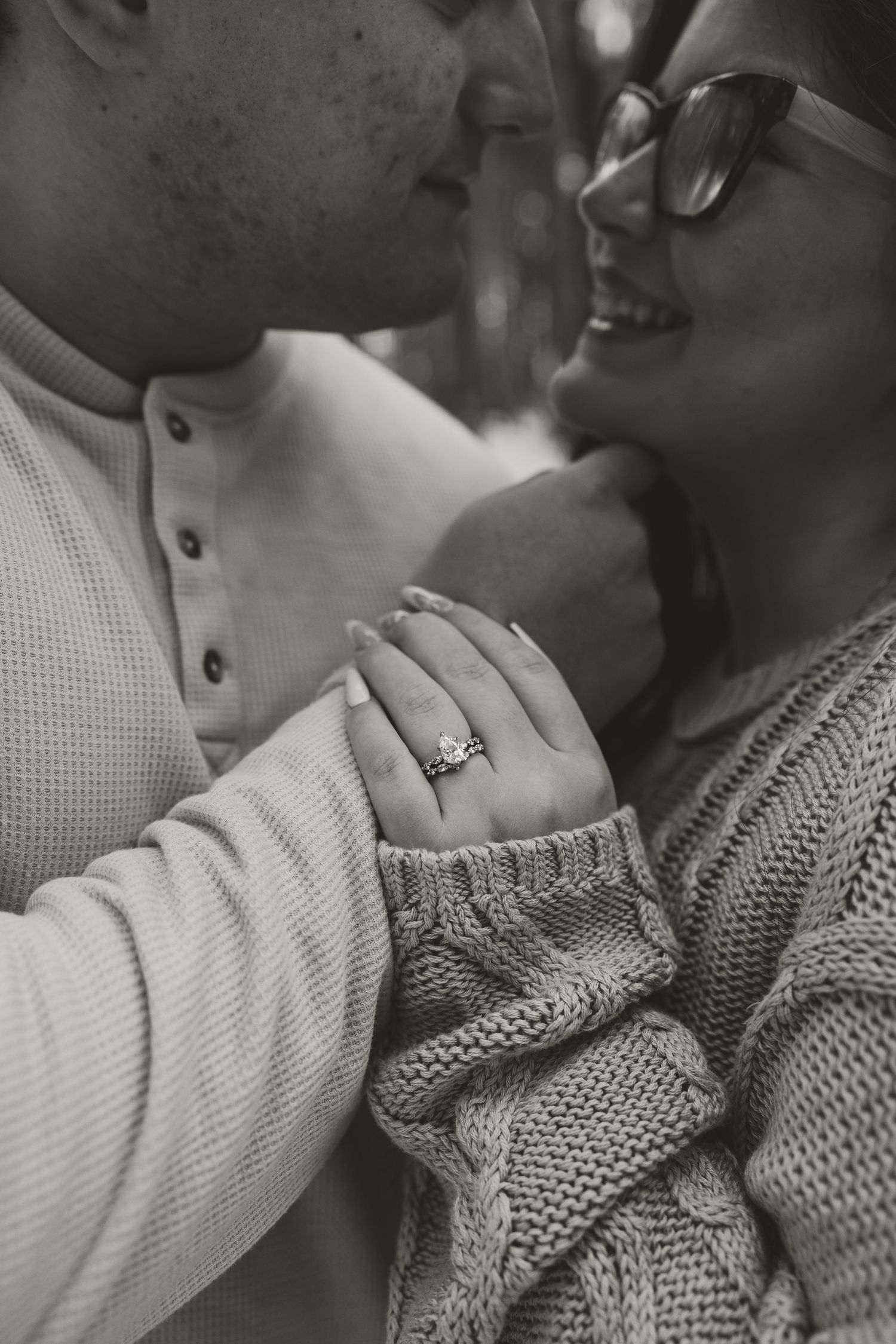 Black and white photo of a couple sharing a kiss, woman showing off her diamond engagement ring, in Grand Rapids, Michigan.