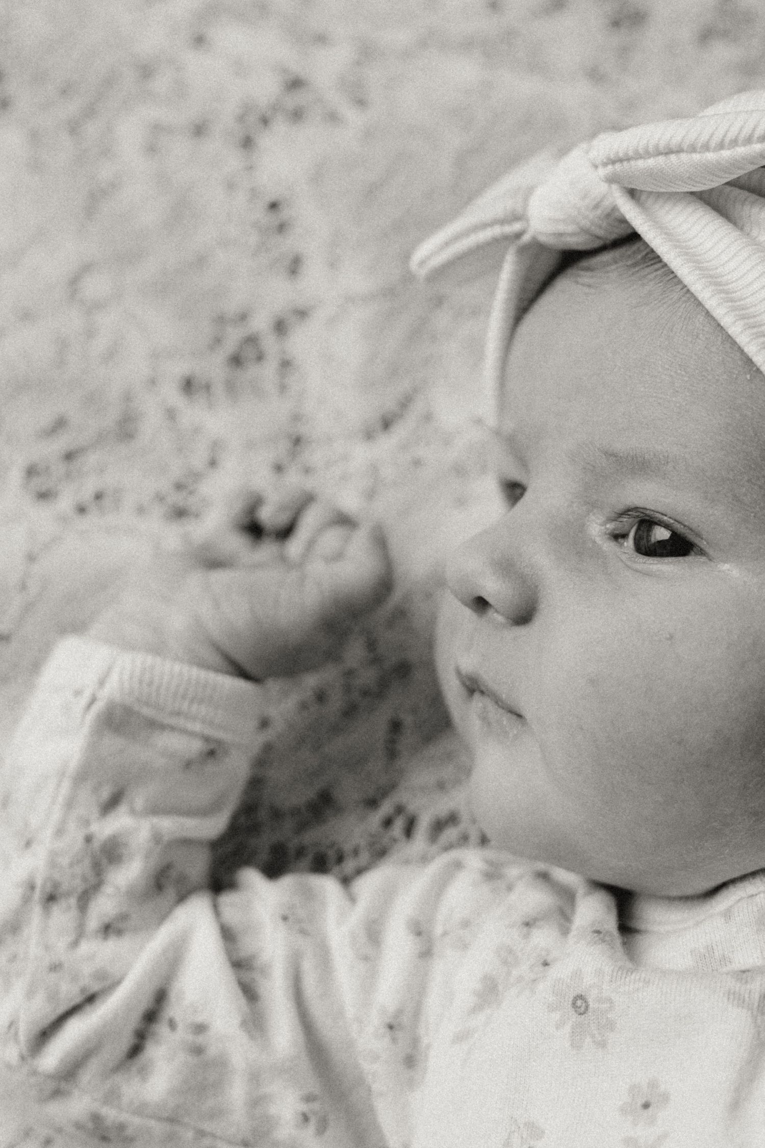 Black and white photo of a cute baby girl wearing a bow headband, lying down and raising her tiny fist.