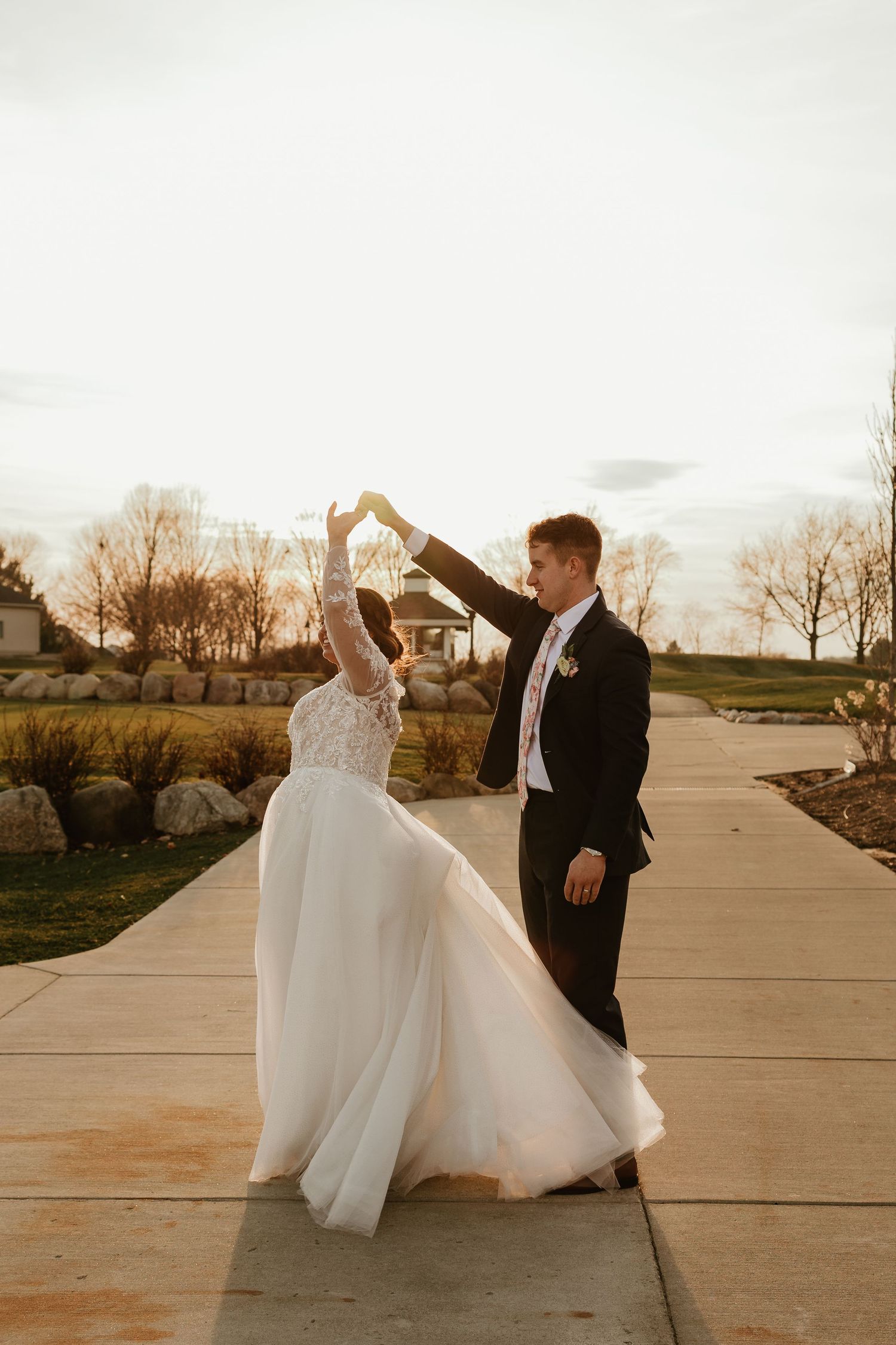A bride and groom share a romantic dance outdoors at golden hour, with the bride's flowing white gown twirling gracefully.