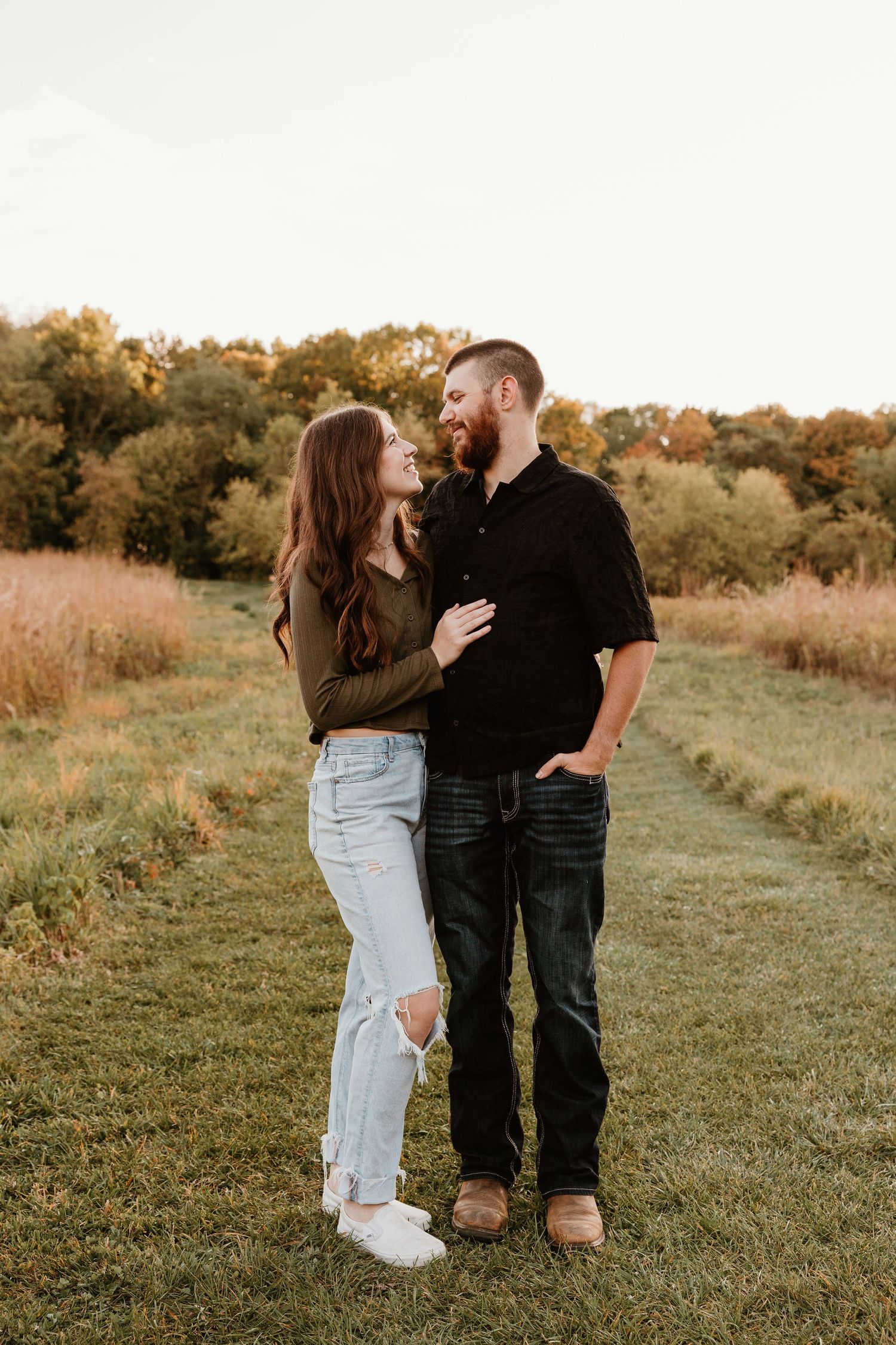 Couple sharing a romantic moment in a sunlit grassy field, woman in ripped jeans and man in black shirt.