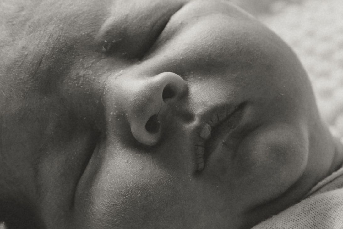 Close-up black and white photo of a sleeping newborn baby's face with soft delicate features.