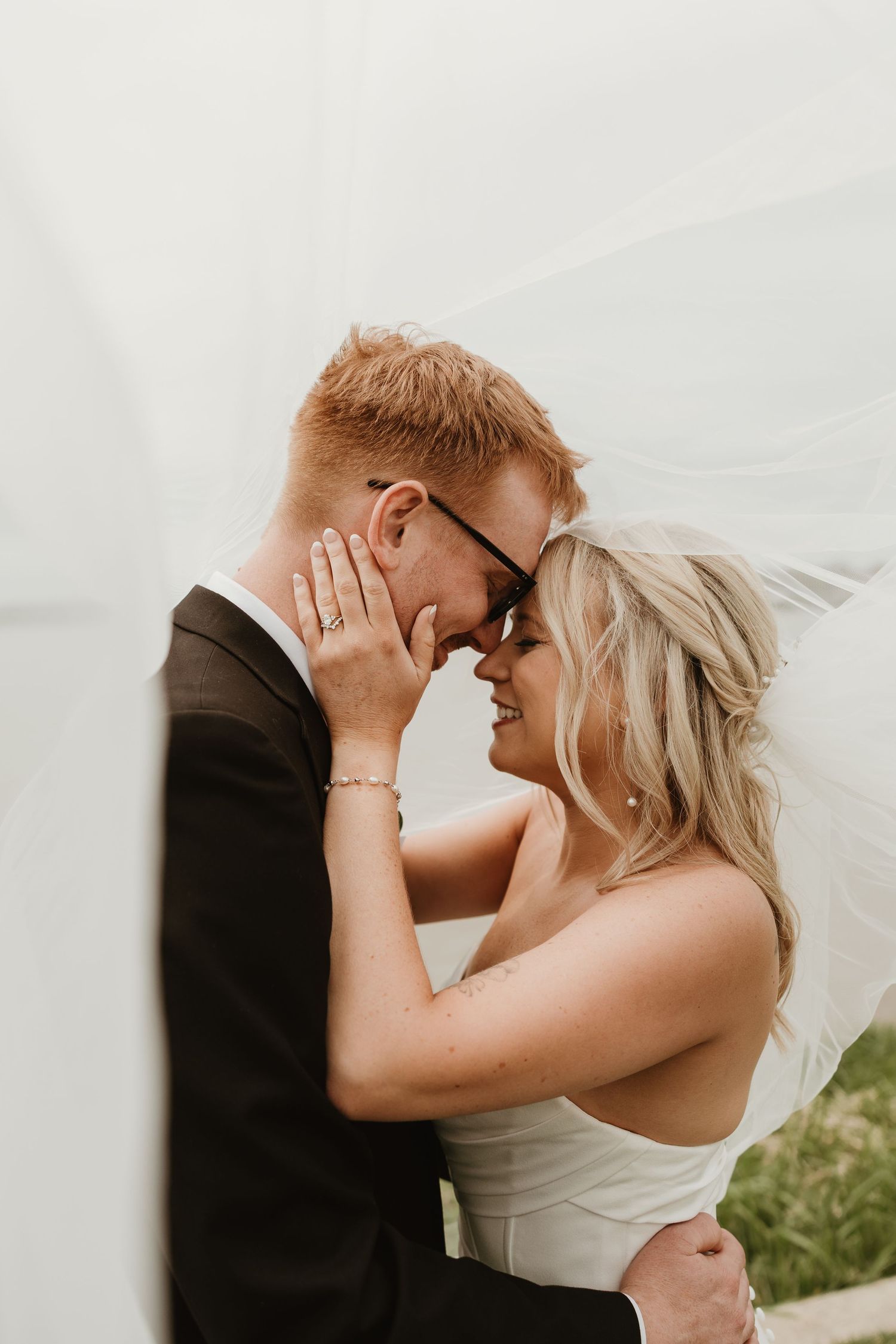 A bride and groom share a romantic forehead touch under a flowing veil on their wedding day.