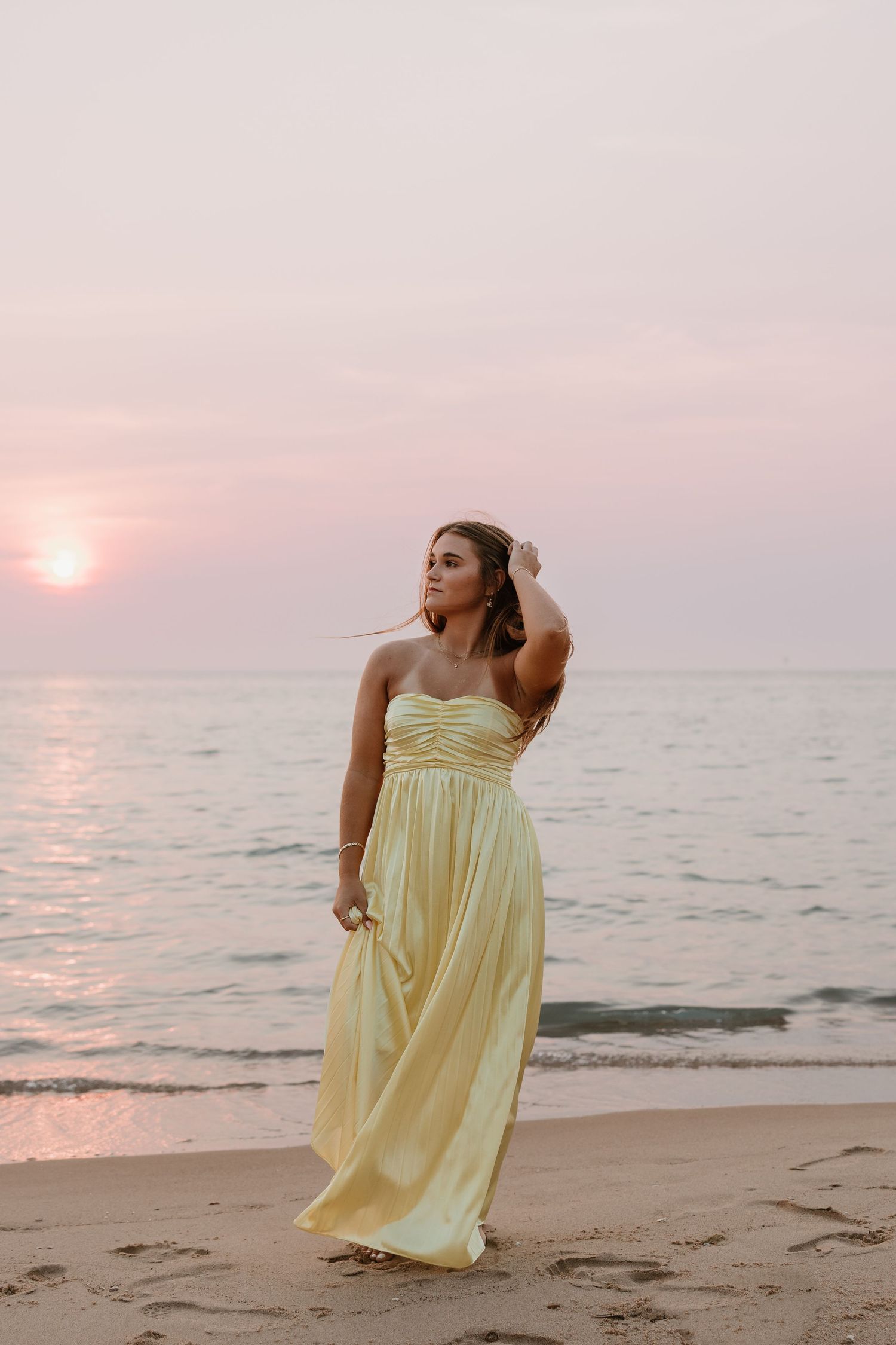 Woman in yellow maxi dress standing on beach at sunset.