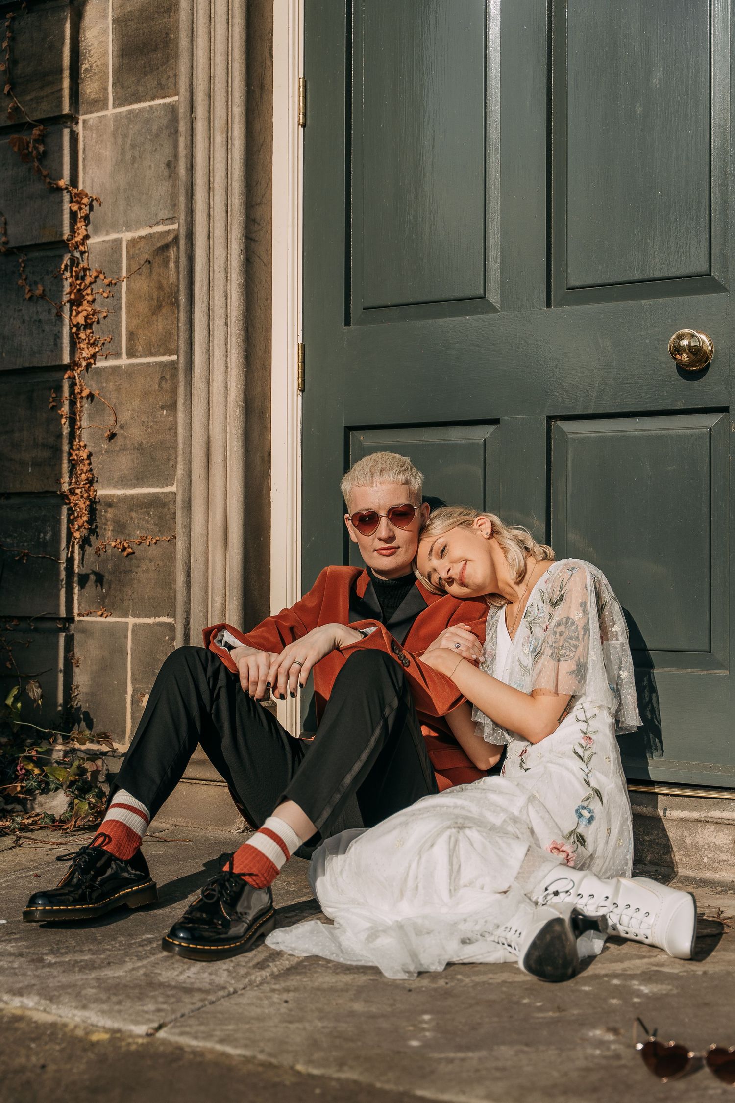 Two Bride's sit on doorstep in the sun, one with glasses and one without, in Hexham.