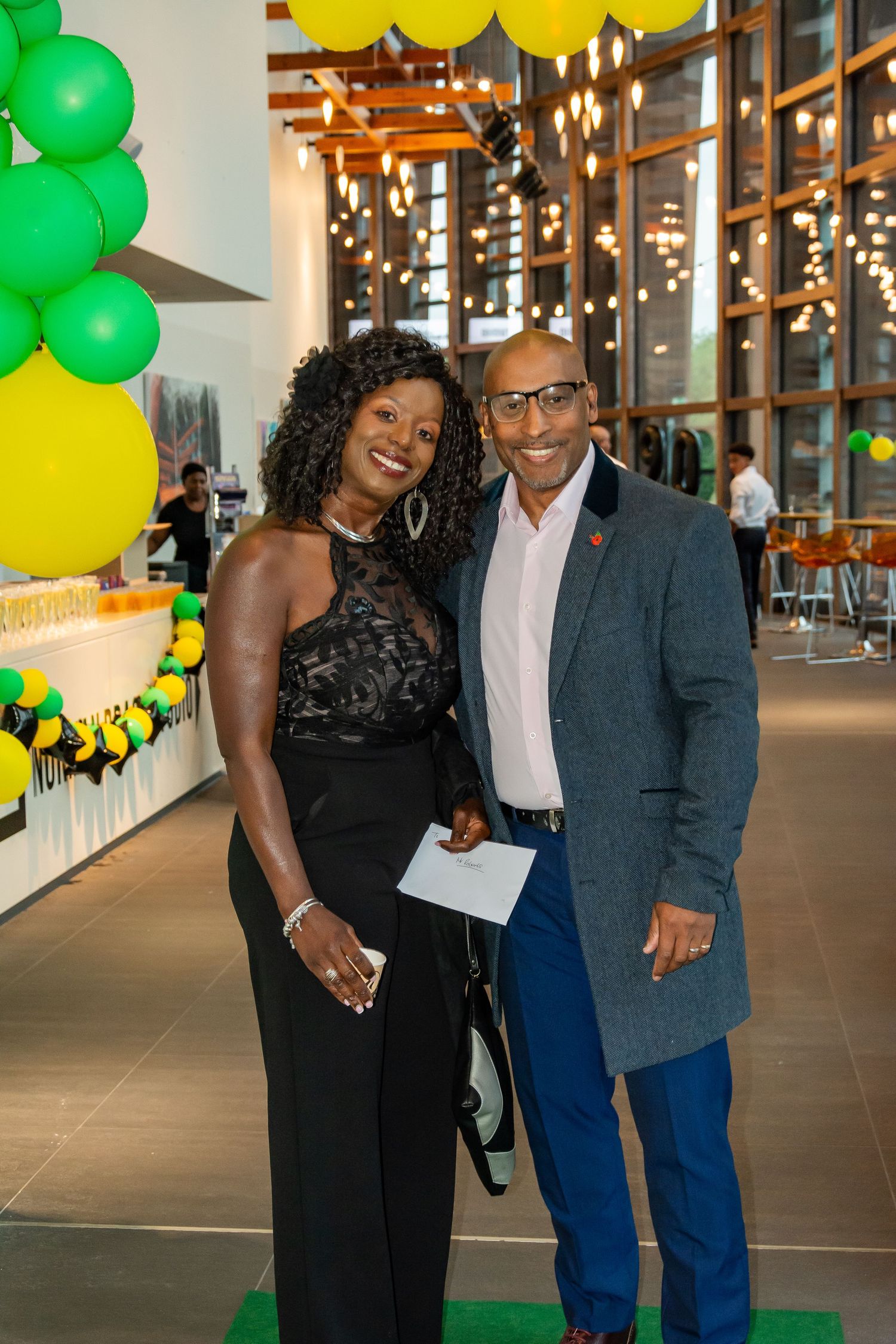 Elegant couple posing together at a festive event with green and yellow balloon decorations.