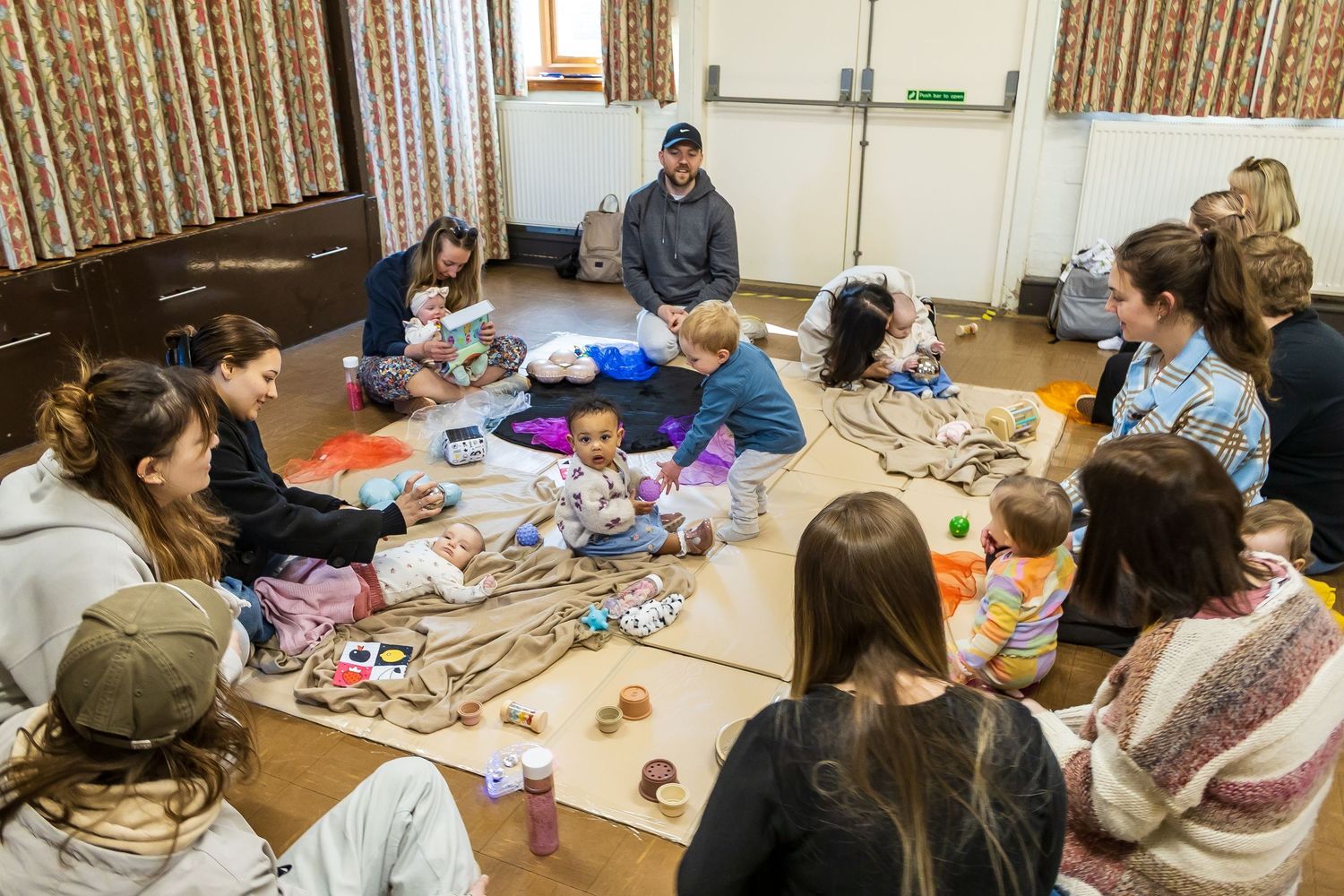 Parents and babies sitting in a circle on the floor during a mother and baby group session.