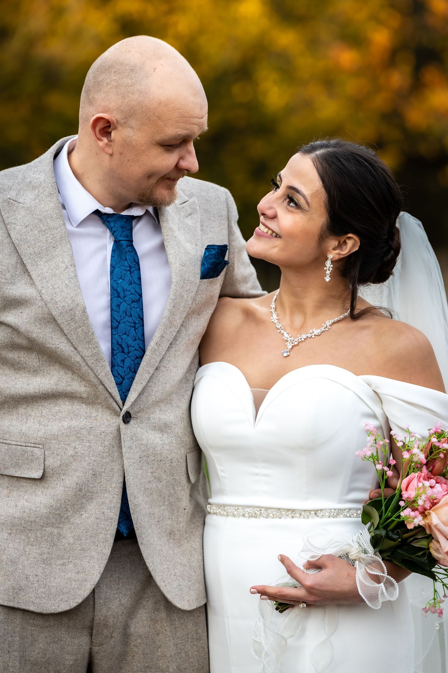 Smiling bride and groom in grey suit sharing a loving look at autumn wedding.