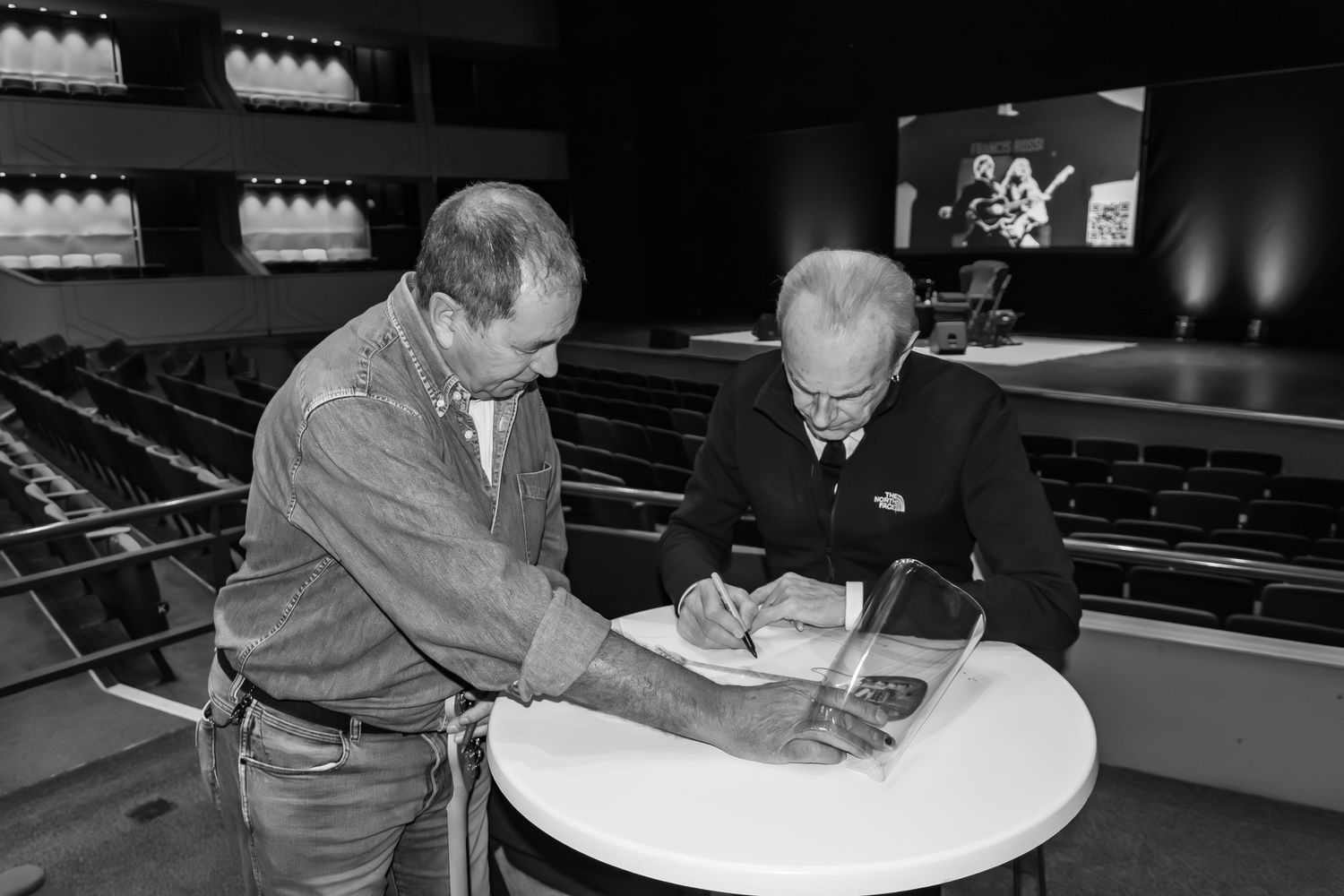 Two men reviewing documents at a round table in a black and white theater photo.