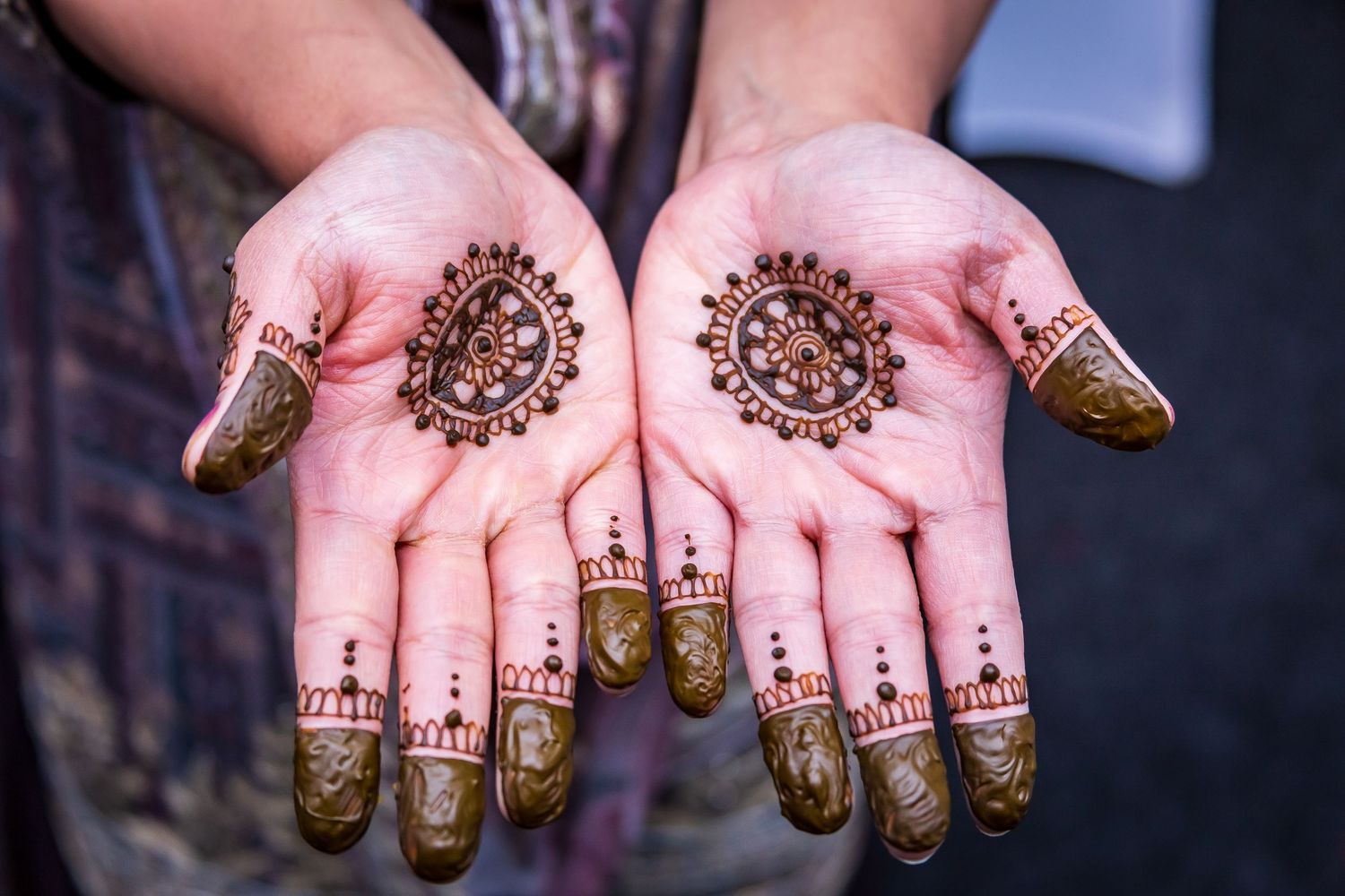 Close-up of a pair of hands displaying intricate henna mehndi designs on the palms and fingertips.