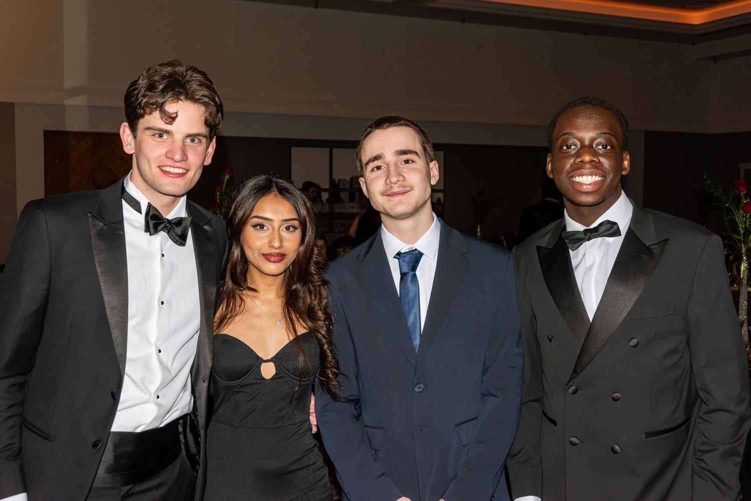 Four elegantly dressed young people posing together at a school ball.