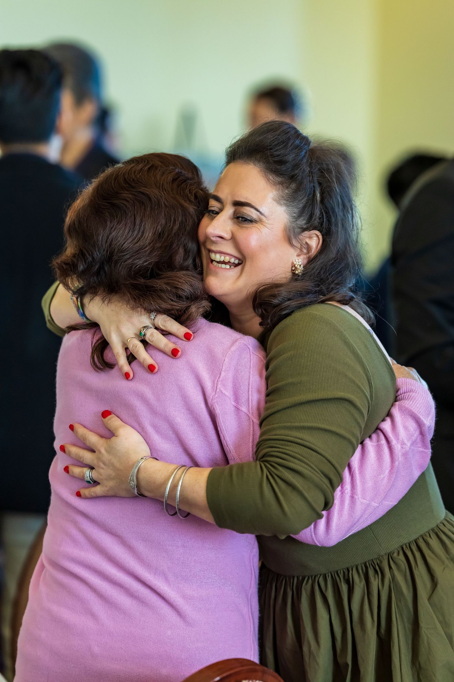 Two women sharing a warm embrace and laughing at a social gathering.