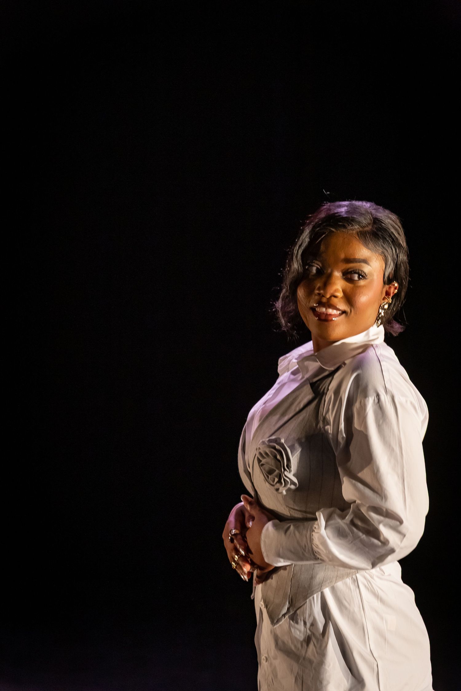 Elegant woman modelling in white button-up outfit posing against dark background in dramatic lighting.