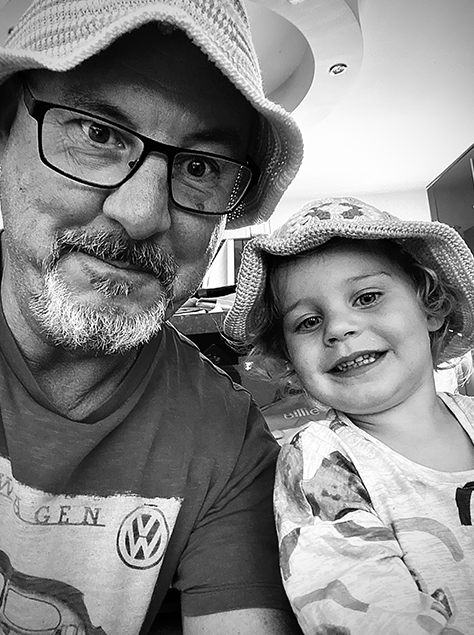 Black and white selfie of a bearded man wearing glasses and a hat with a smiling toddler in a bucket hat.