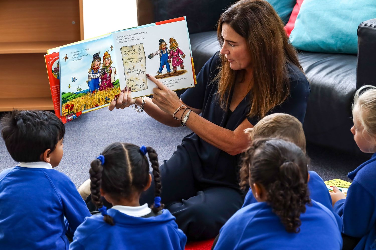 Teacher reading a book to young children in blue school uniforms.