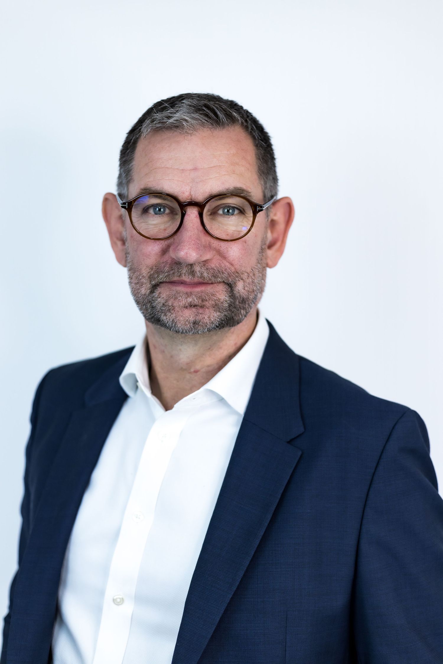 Professional headshot of a middle-aged businessman wearing glasses and navy blazer on white background.