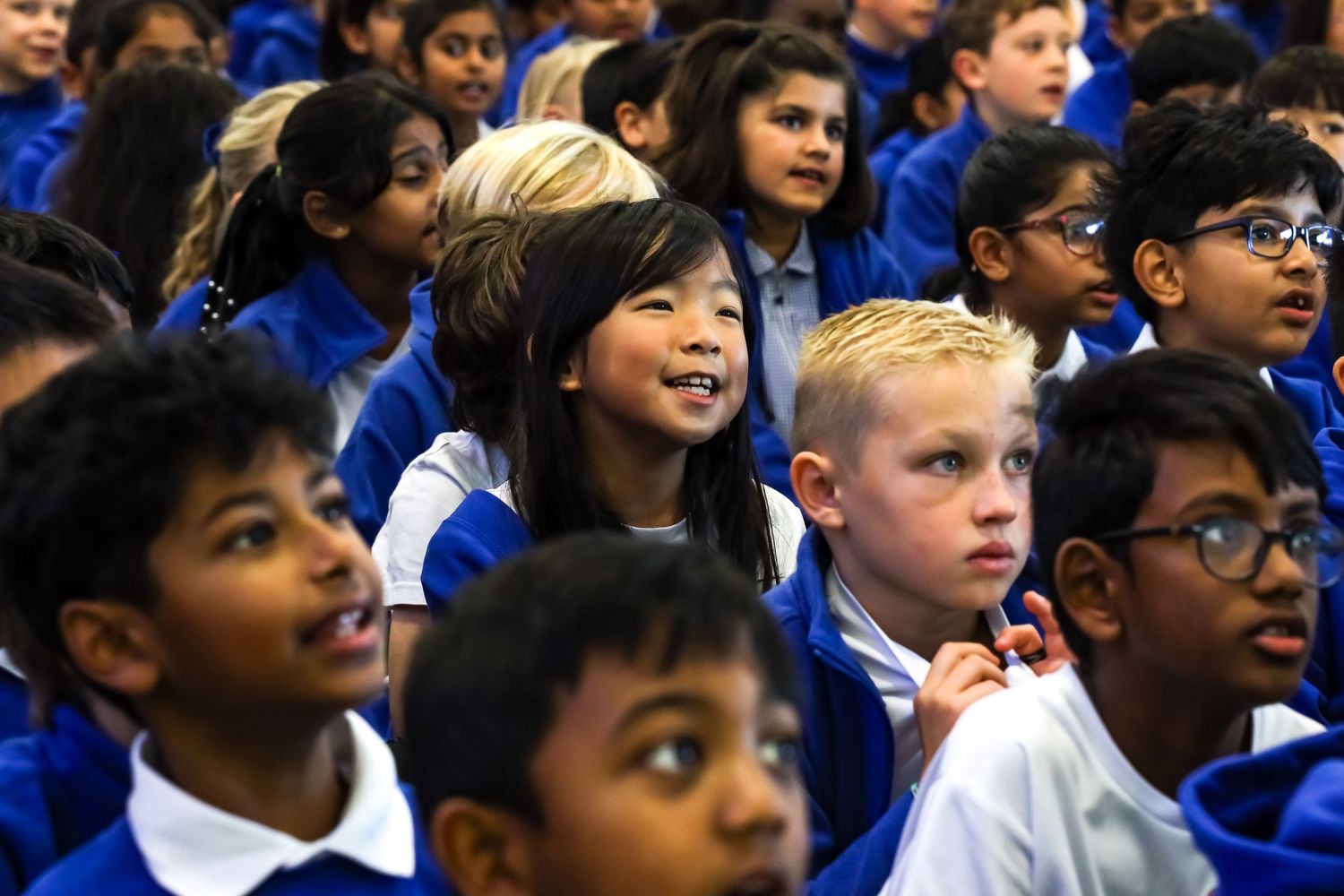 Diverse group of primary school children in blue uniforms sitting together at a school assembly. School photography done by LJPhotostop
