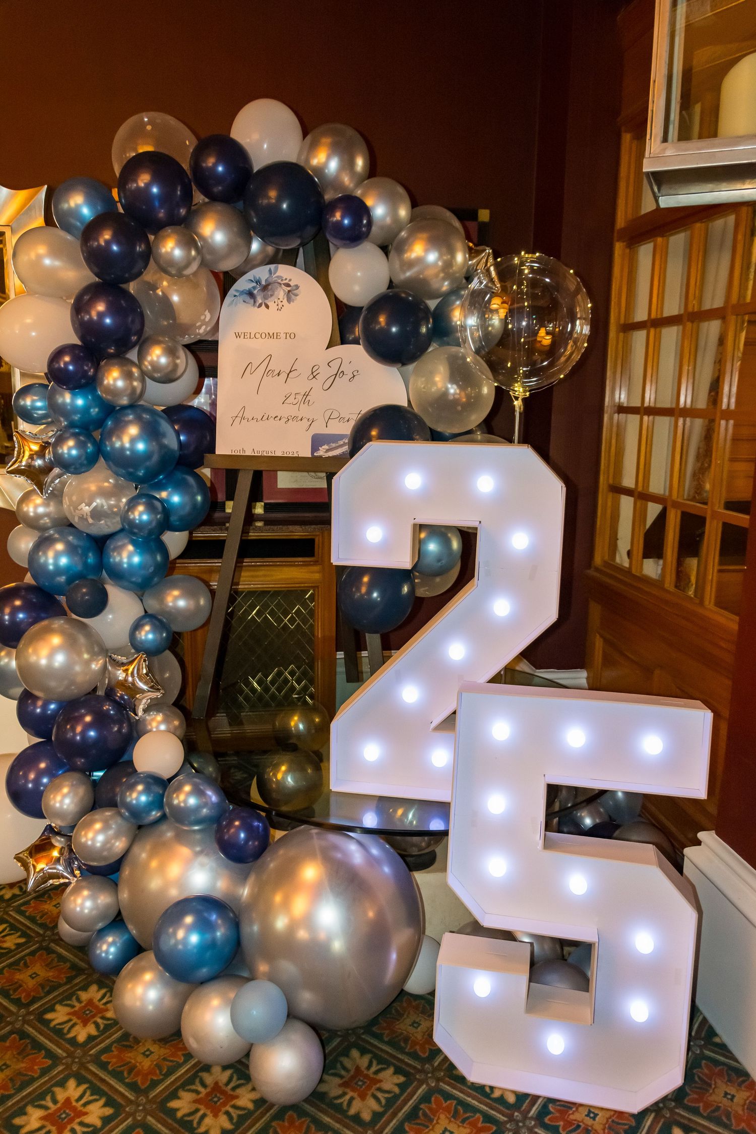 Blue and silver balloon arch with illuminated marquee number 25 for a anniversary party celebration.